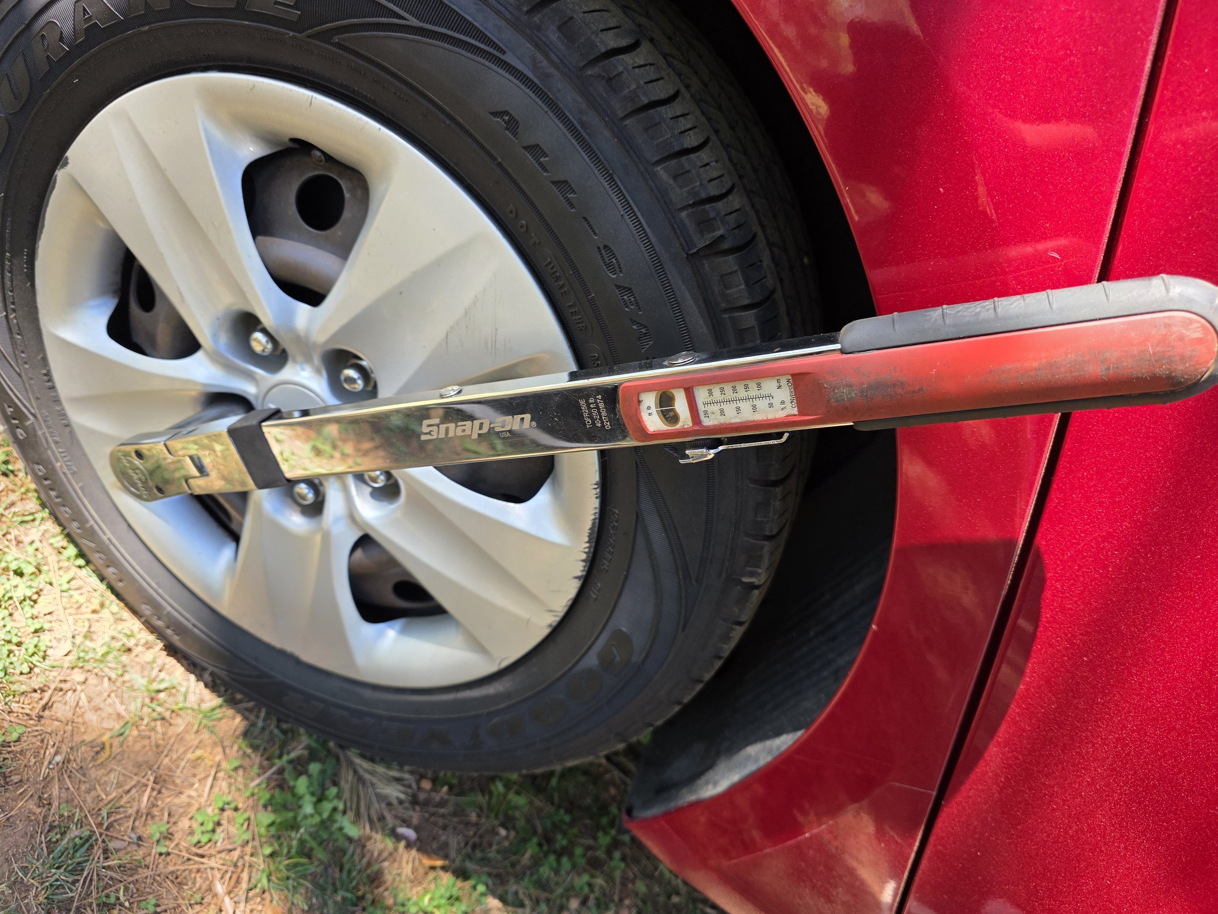 Red car with a silver hubcap on the wheel, a black tire, and a metal level placed against the tire, showing the car's wheel alignment.