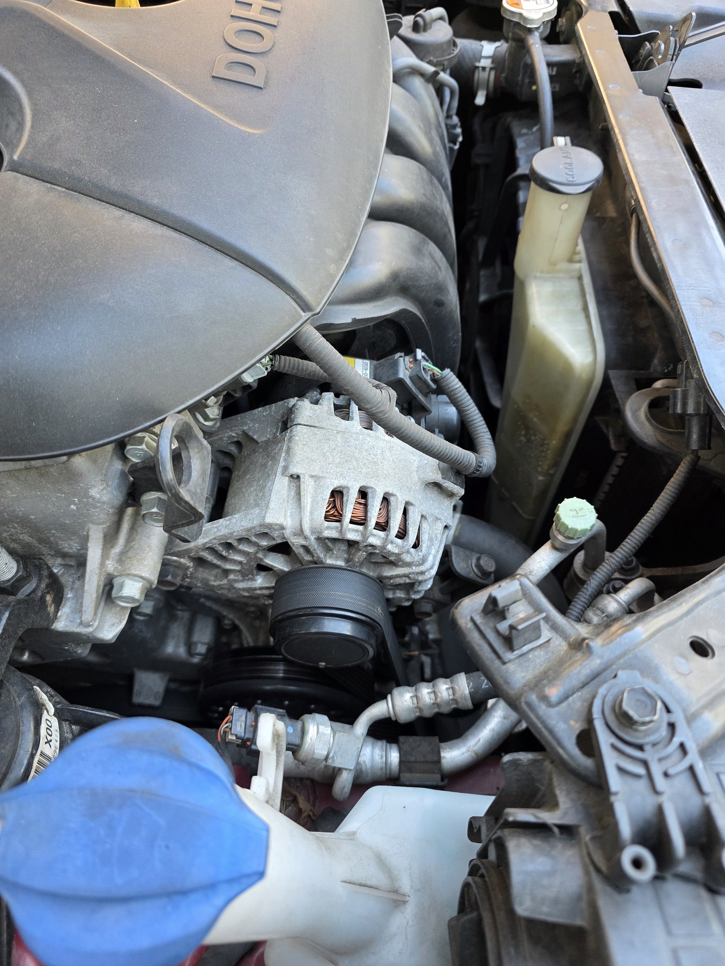Close-up view of a car engine showing various components including the alternator, serpentine belt, radiator, and parts of the engine bay.