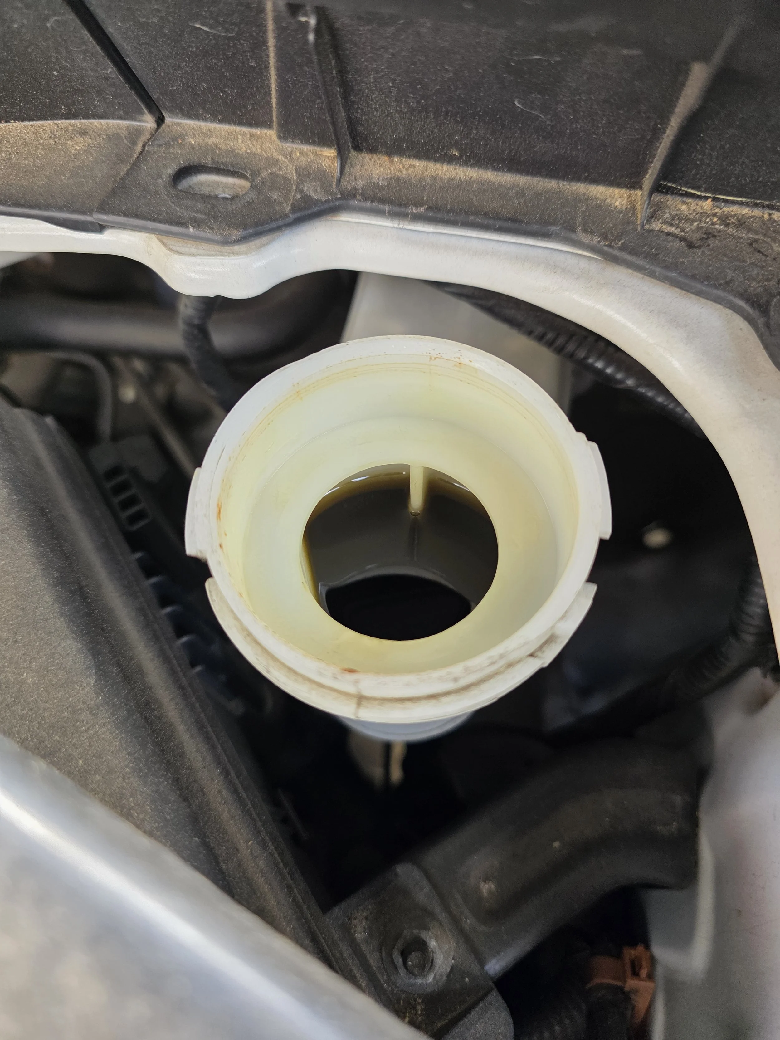 Open brake fluid reservoir with dark brown brake fluid inside in a car engine bay.