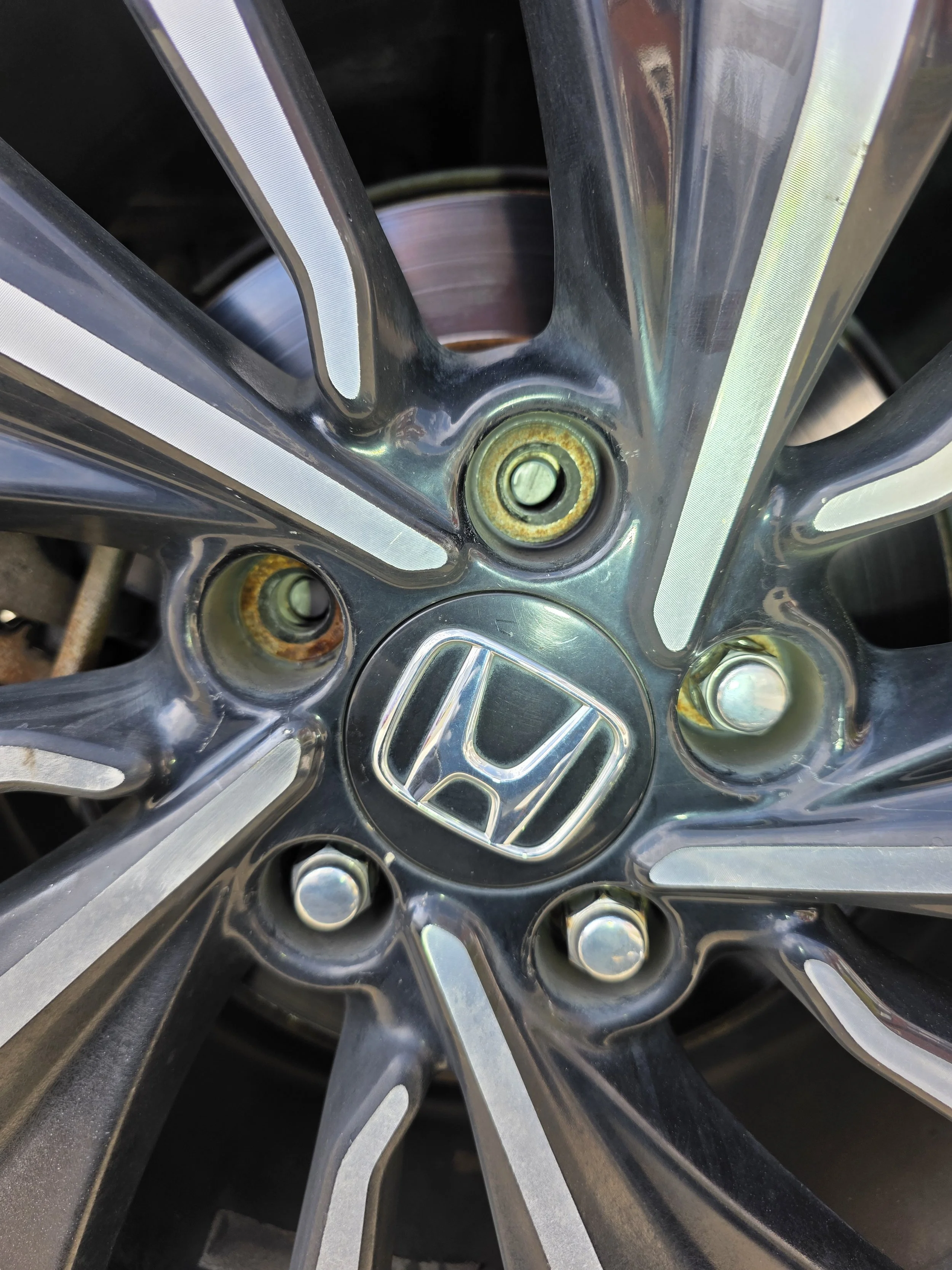 Close-up of a Honda car wheel rim with the Honda logo in the center, showing lug holes and some rust around the edges.