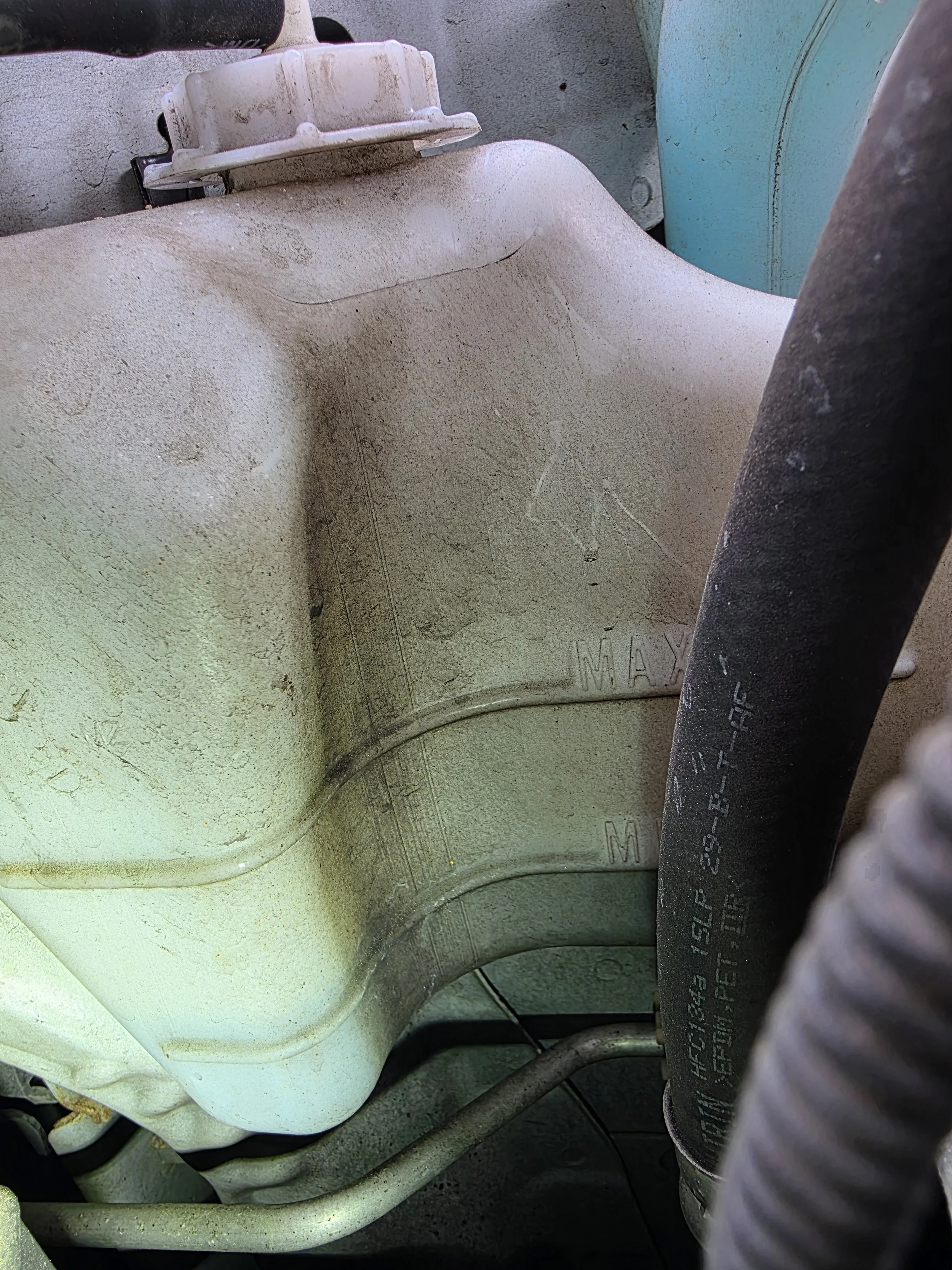 Close-up of a dusty, white plastic container or reservoir with measurement markings and a black hose attached.