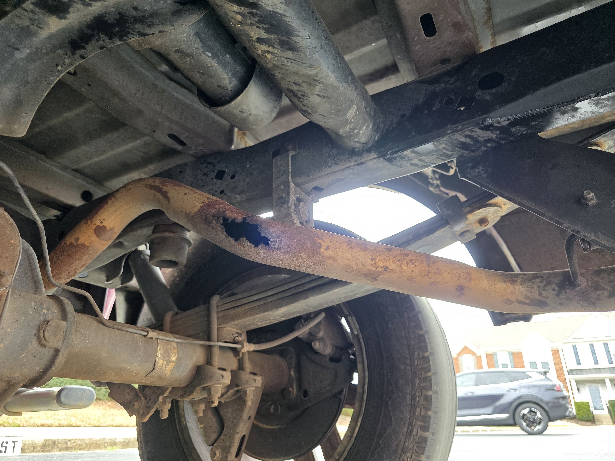 Underneath view of a vehicle showing rusted frame, suspension, tire, and undercarriage components.