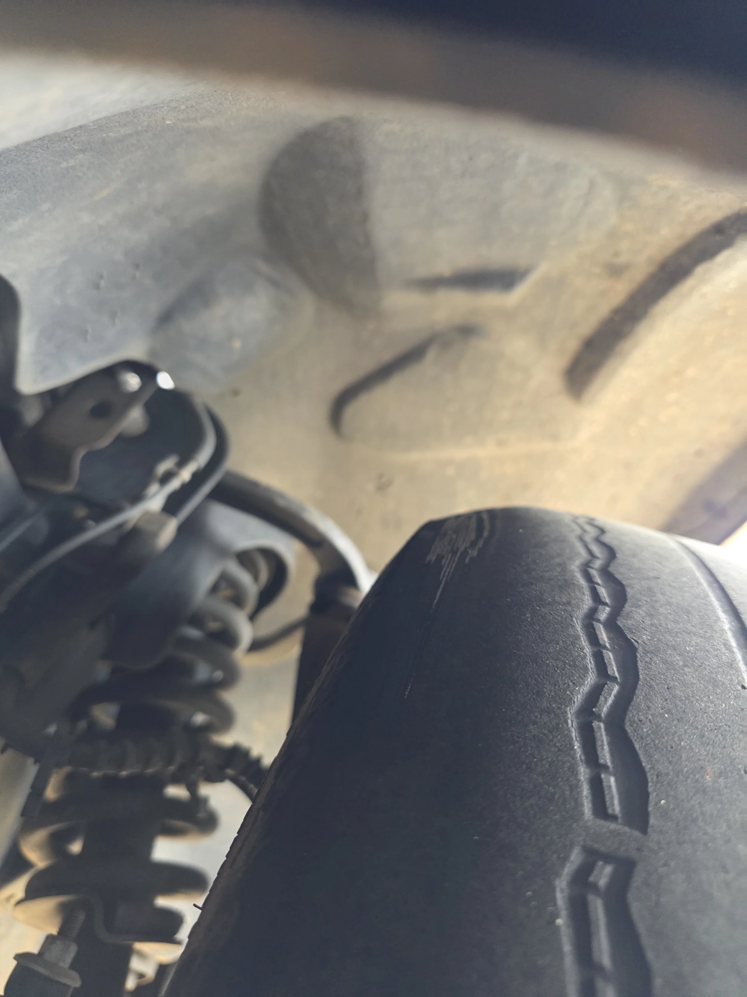 Close-up view of a vehicle's suspension system and tire, showing a worn tire tread and suspension components.