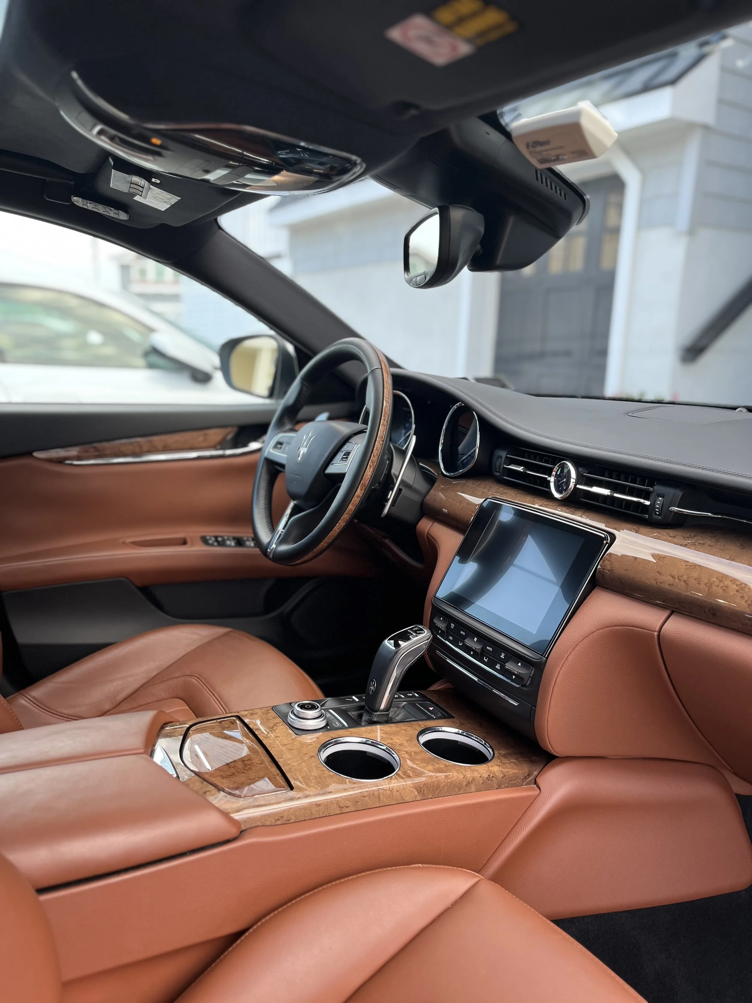 The interior of a luxury car featuring a brown leather dashboard and seats, a wood trim center console with cup holders, a touchscreen display, a gear shift, and a steering wheel.