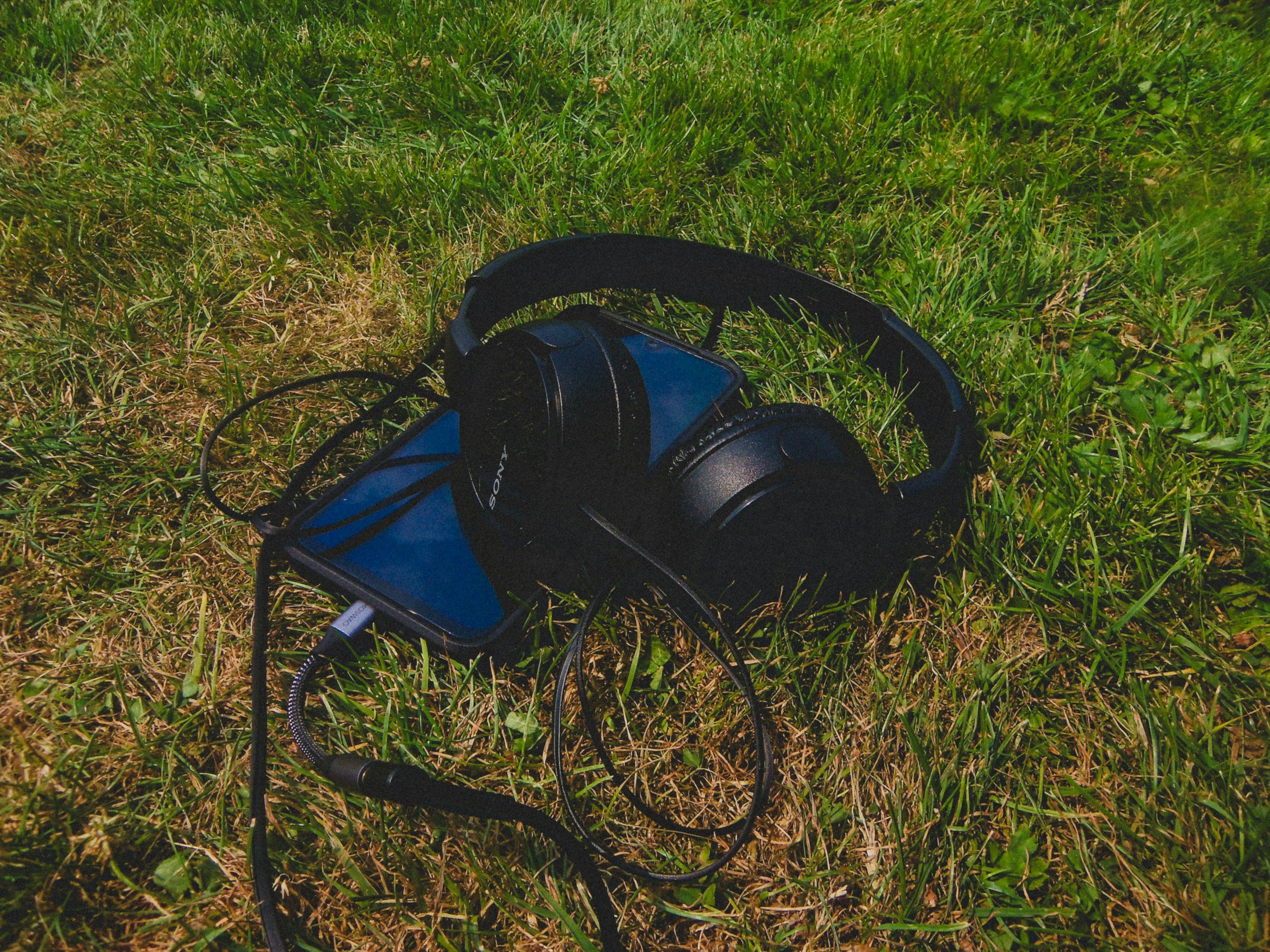 Headphones placed on top of a blue Sony portable speaker on green grass.