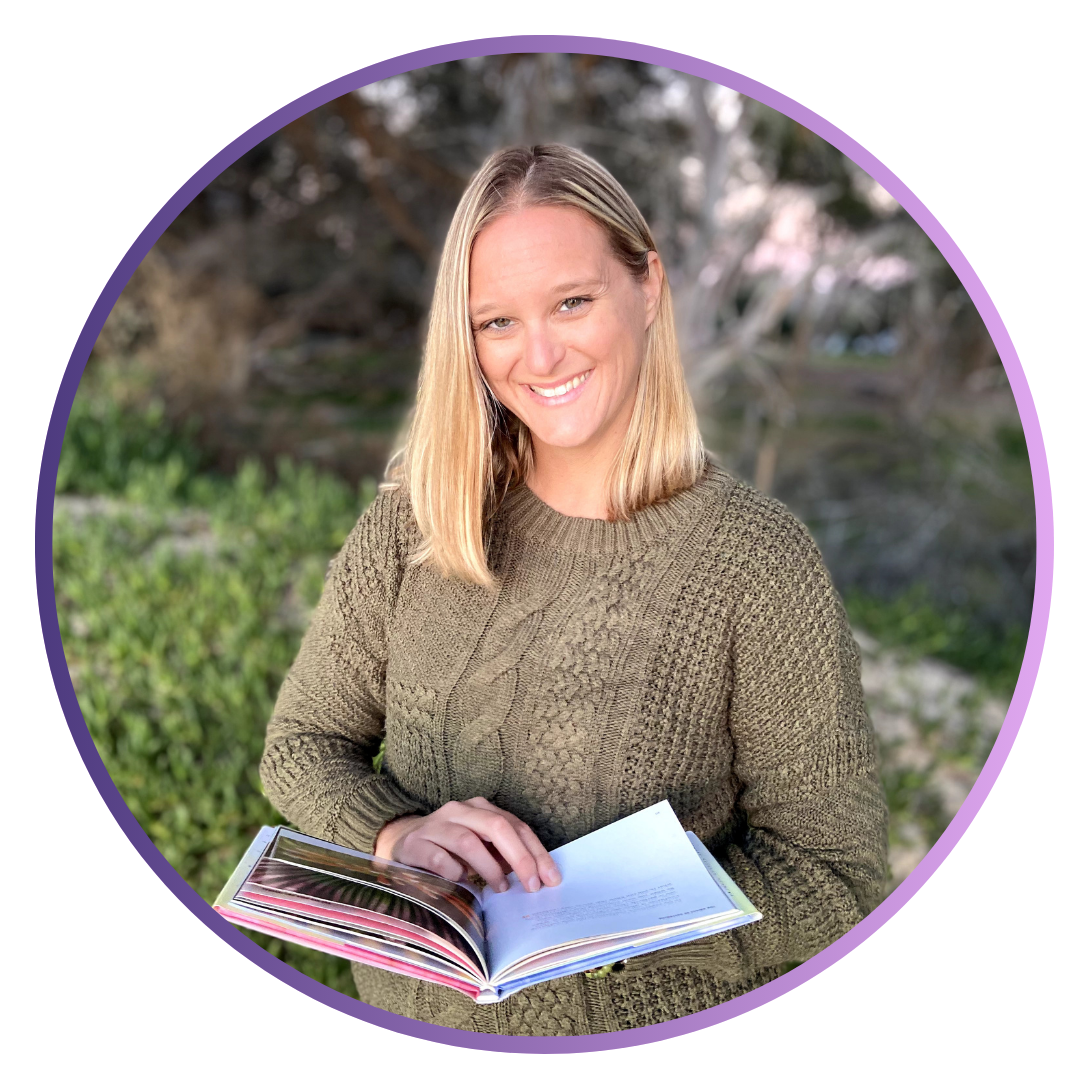 A smiling woman with blonde hair wearing a green knitted sweater, holding an open book outdoors in a natural setting with trees and greenery in the background.