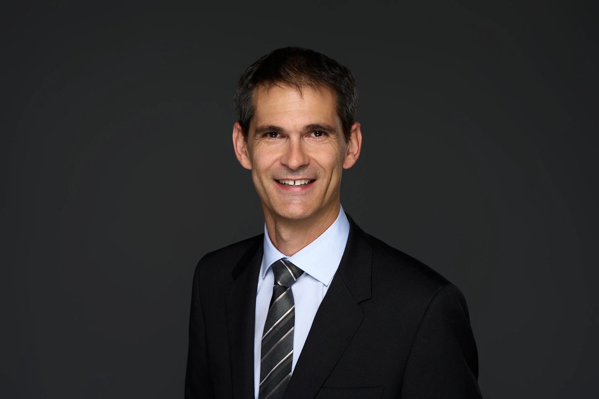 NYC headshot Photography featuring a confident business CEO leader in a dark suit against a dark background