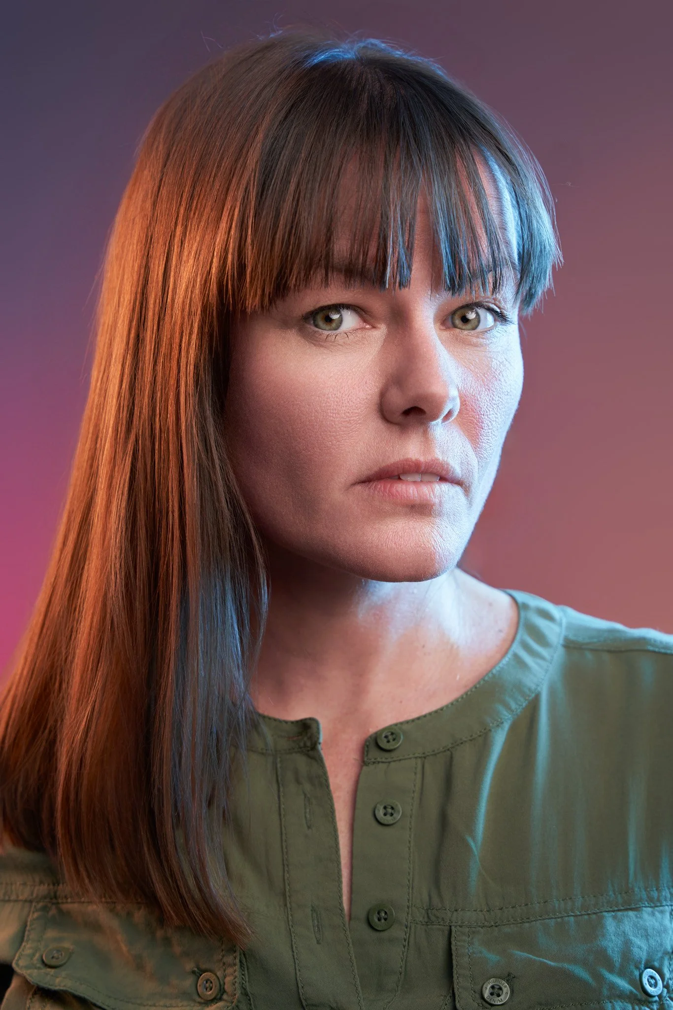 Actor headshot of a woman with straight brown hair and fringe, thoughtful and composed expression, wearing a green top, photographed in a Brooklyn studio with cinematic lighting by an NYC actor headshot photographer.