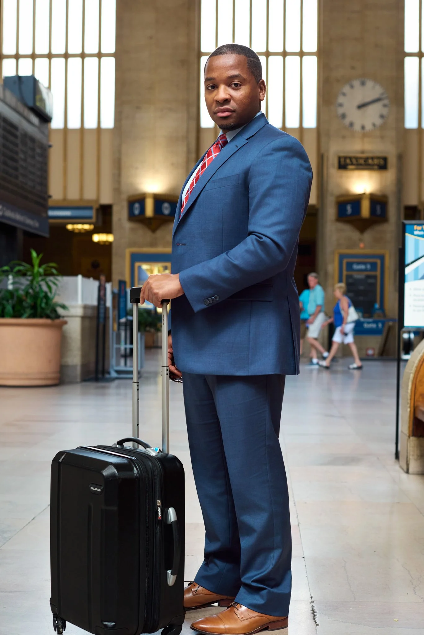 Professional lifestyle portrait of a man in a blue suit standing with his luggage inside an Amtrak station, created for National Magazine by David Pexton Photography