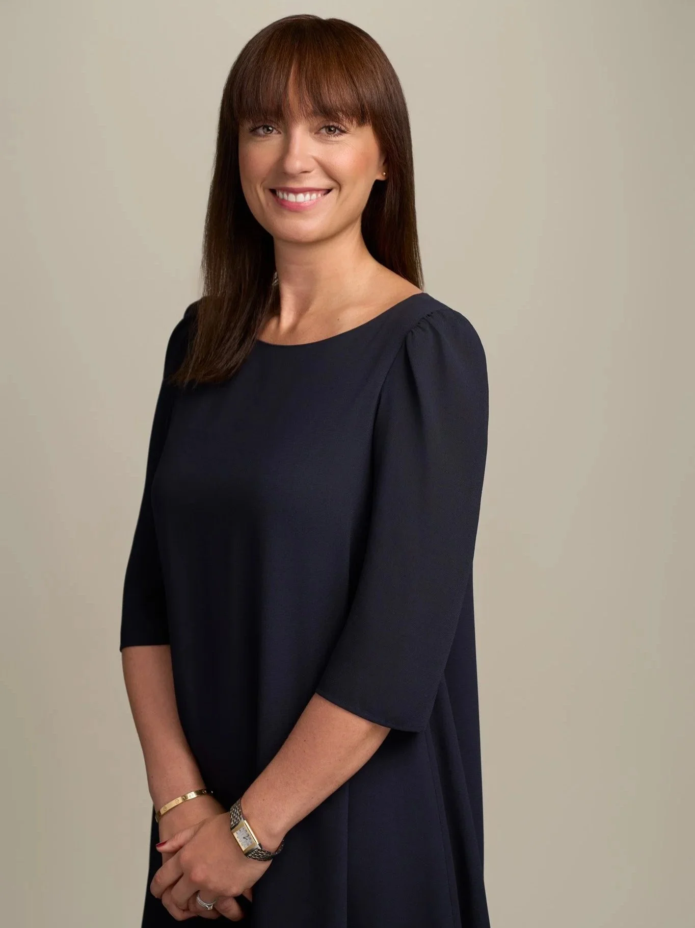 Professional headshot in New York City of a woman in a dark blue dress, photographed against a clean, light studio backdrop