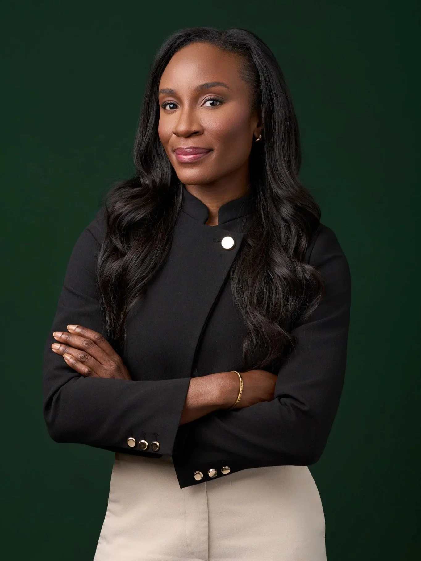 Executive headshot of a woman in a black blazer with arms crossed against a deep green background, confident expression with soft studio lighting, David Pexton Photography NYC
