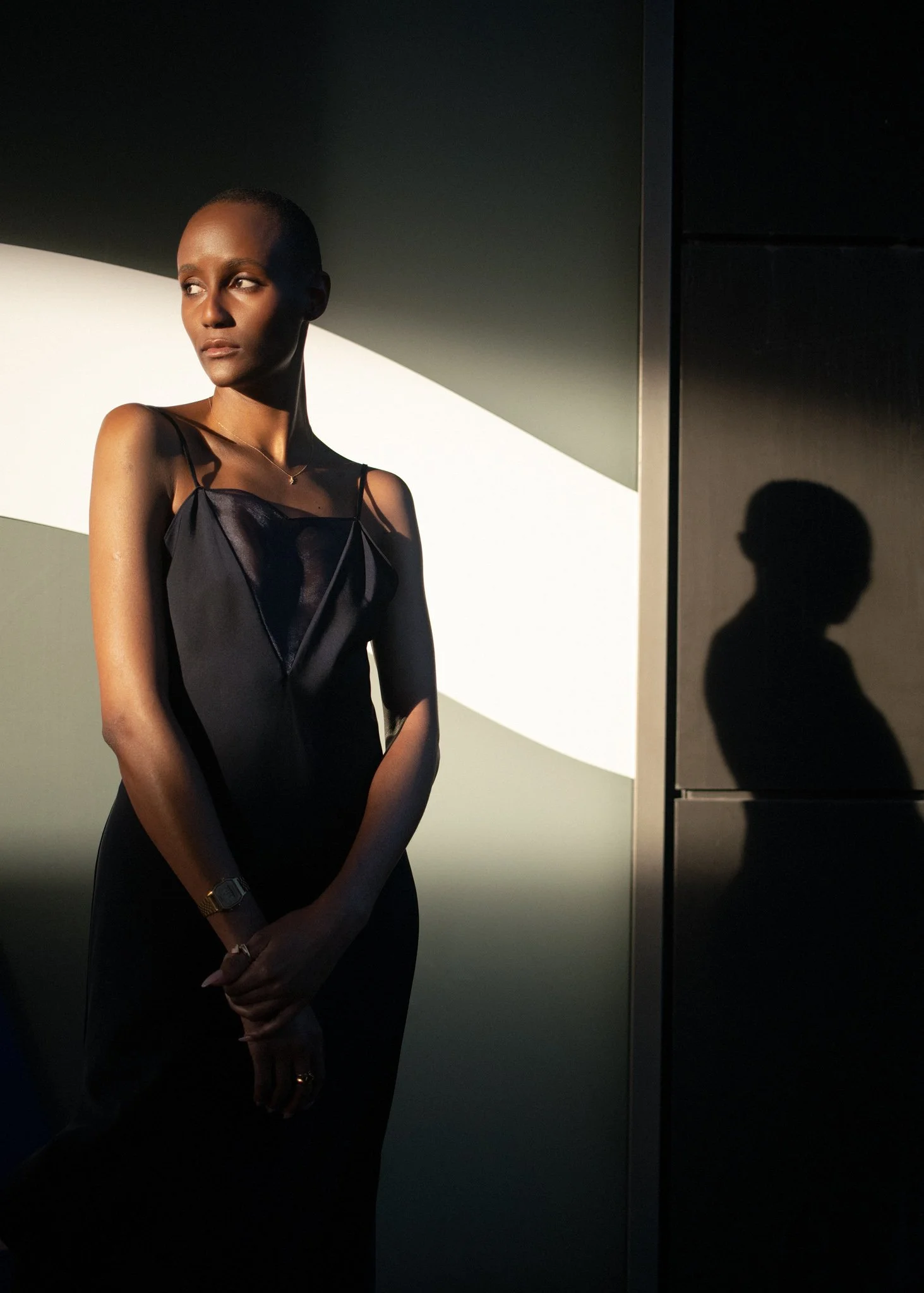 Natural light portraits in New York City featuring a woman in a black dress standing against a modern backdrop, her shadow cast beside her in warm evening light — minimalist and striking portrait by David Pexton Photography