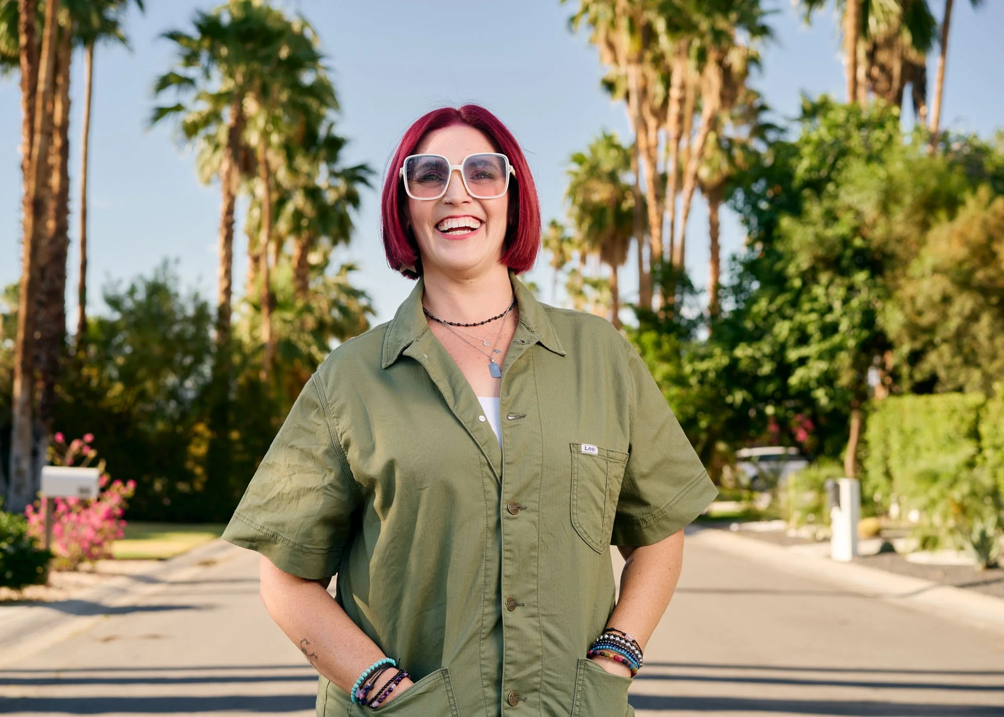 Editorial portrait photographed in Palm Springs of a woman standing in the street lined with palm trees, bright desert sunlight and relaxed California style.