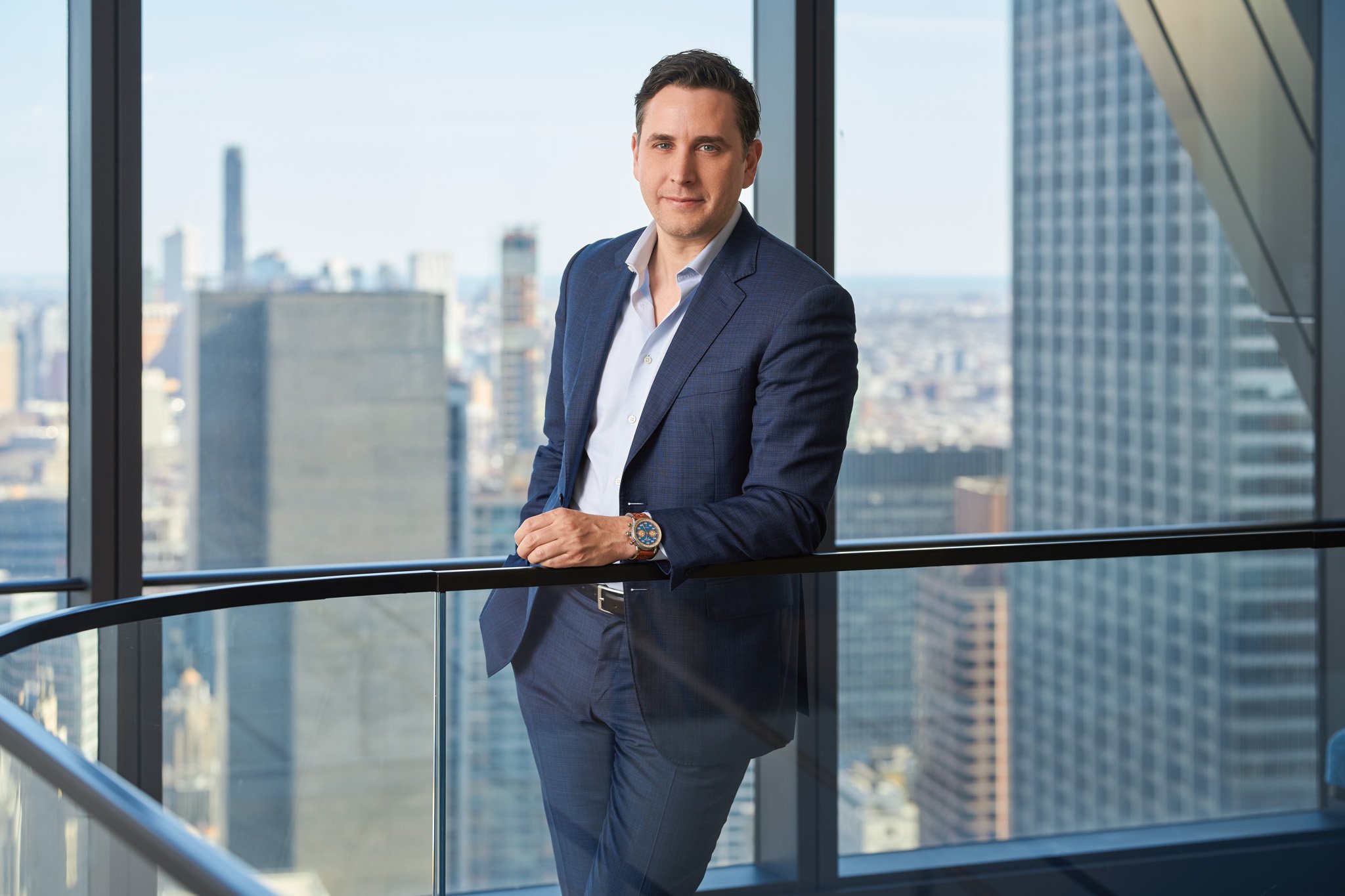 An executive headshot of a law partner stands by a window, overlooking the iconic New York City skyline.