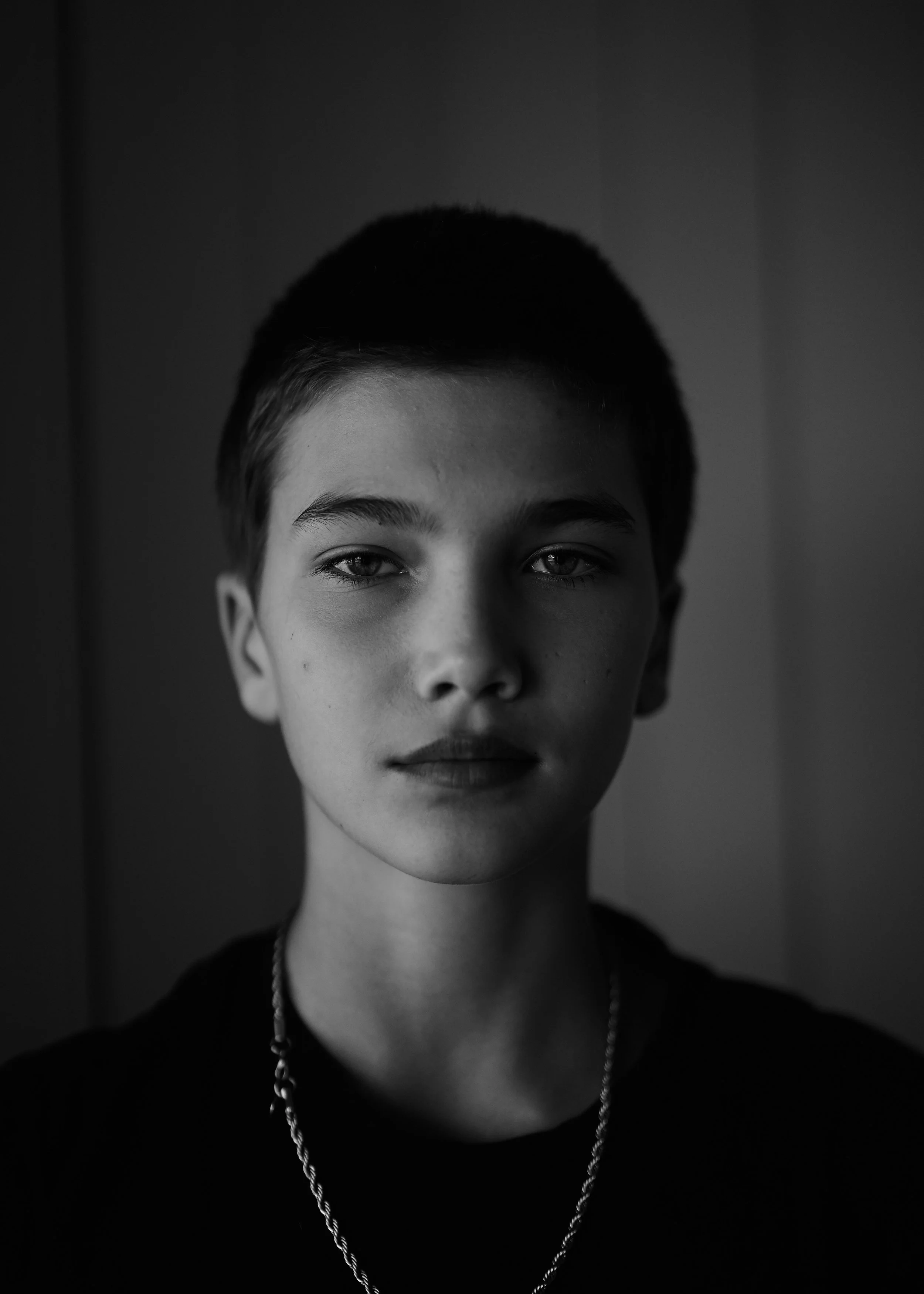Black and white actor headshot of a young performer with short hair, direct gaze and dramatic side lighting creating a moody, cinematic portrait.