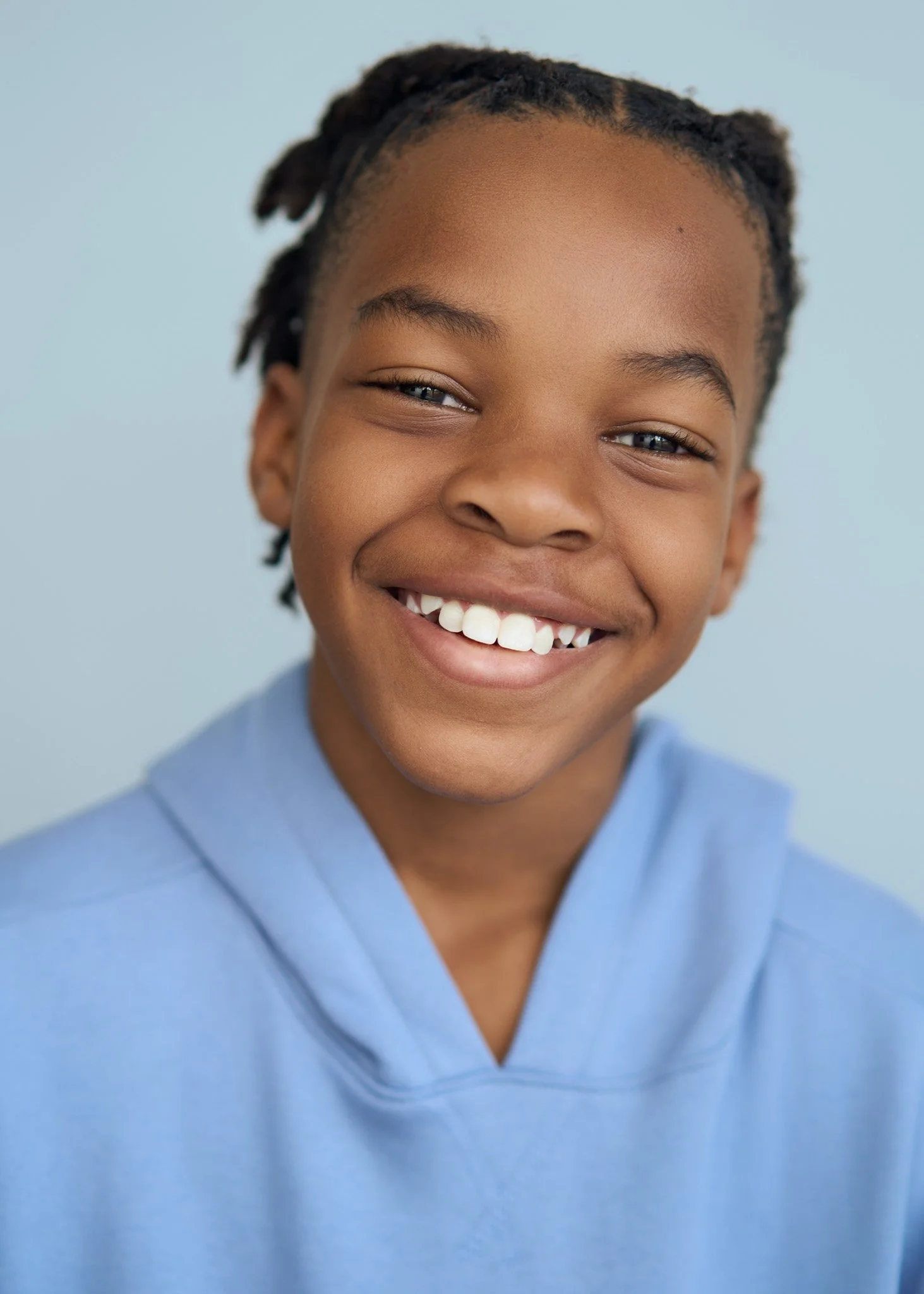 Studio portrait in New York City of a smiling child in a light blue hoodie against a plain background