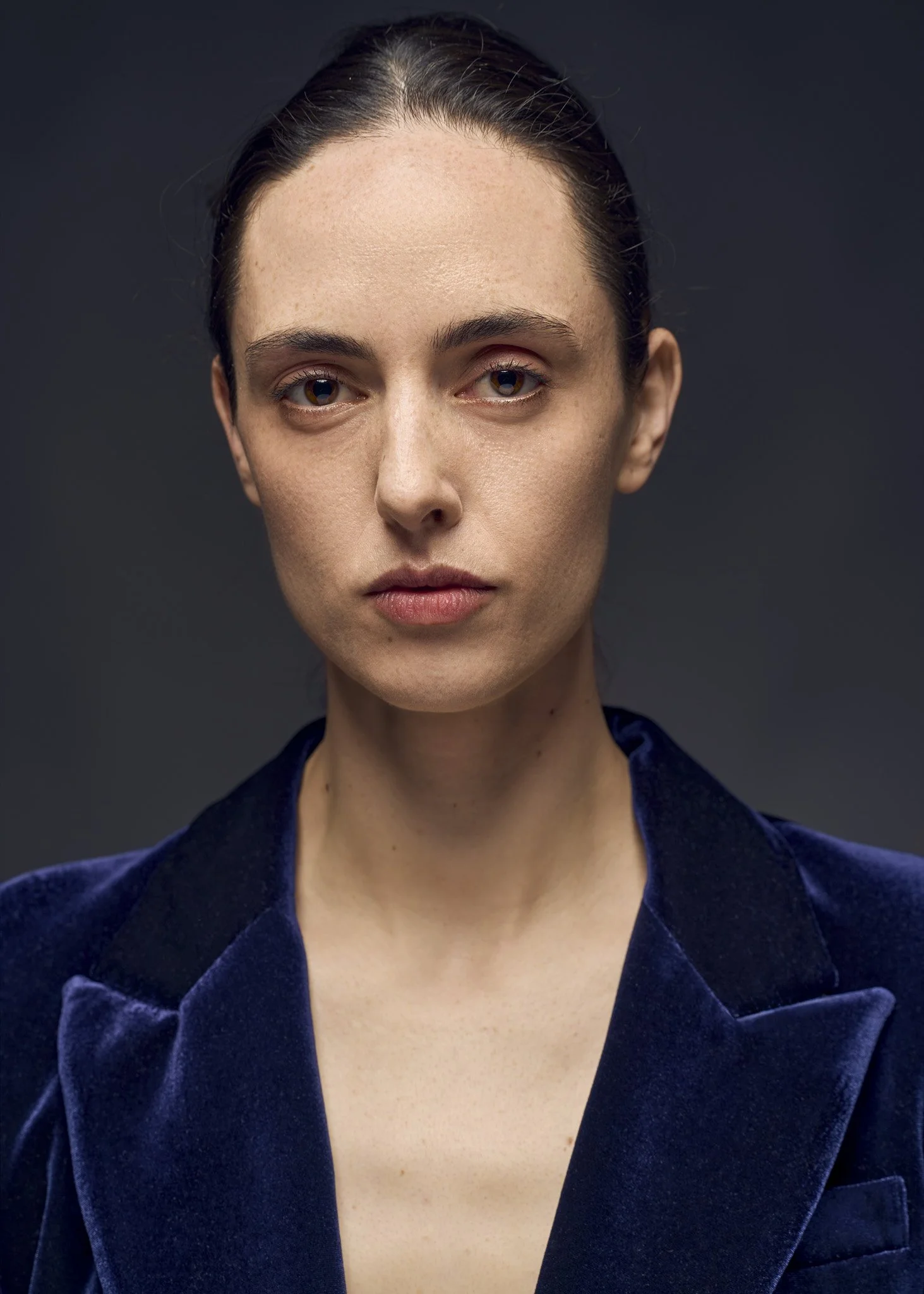 Studio portrait of a woman wearing a deep blue blazer against a dark background, direct gaze, soft controlled lighting and shallow depth of field, photographed in Brooklyn