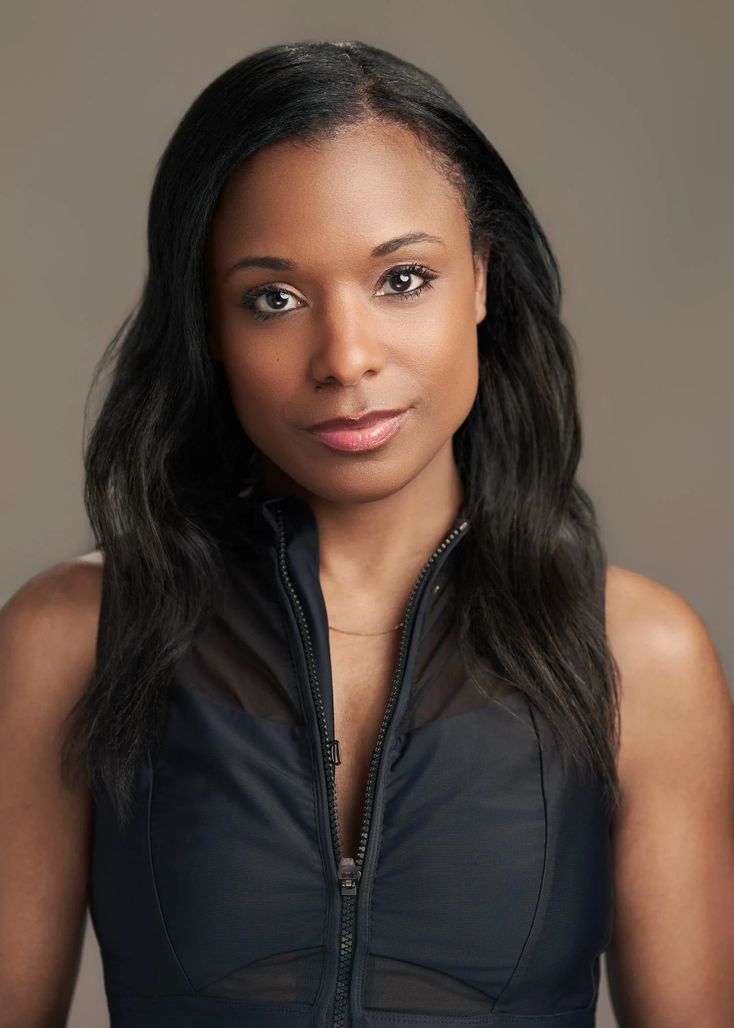 Portrait of a female actor with long black wavy hair photographed in a New York City studio, wearing a sleeveless black top and looking directly at the camera