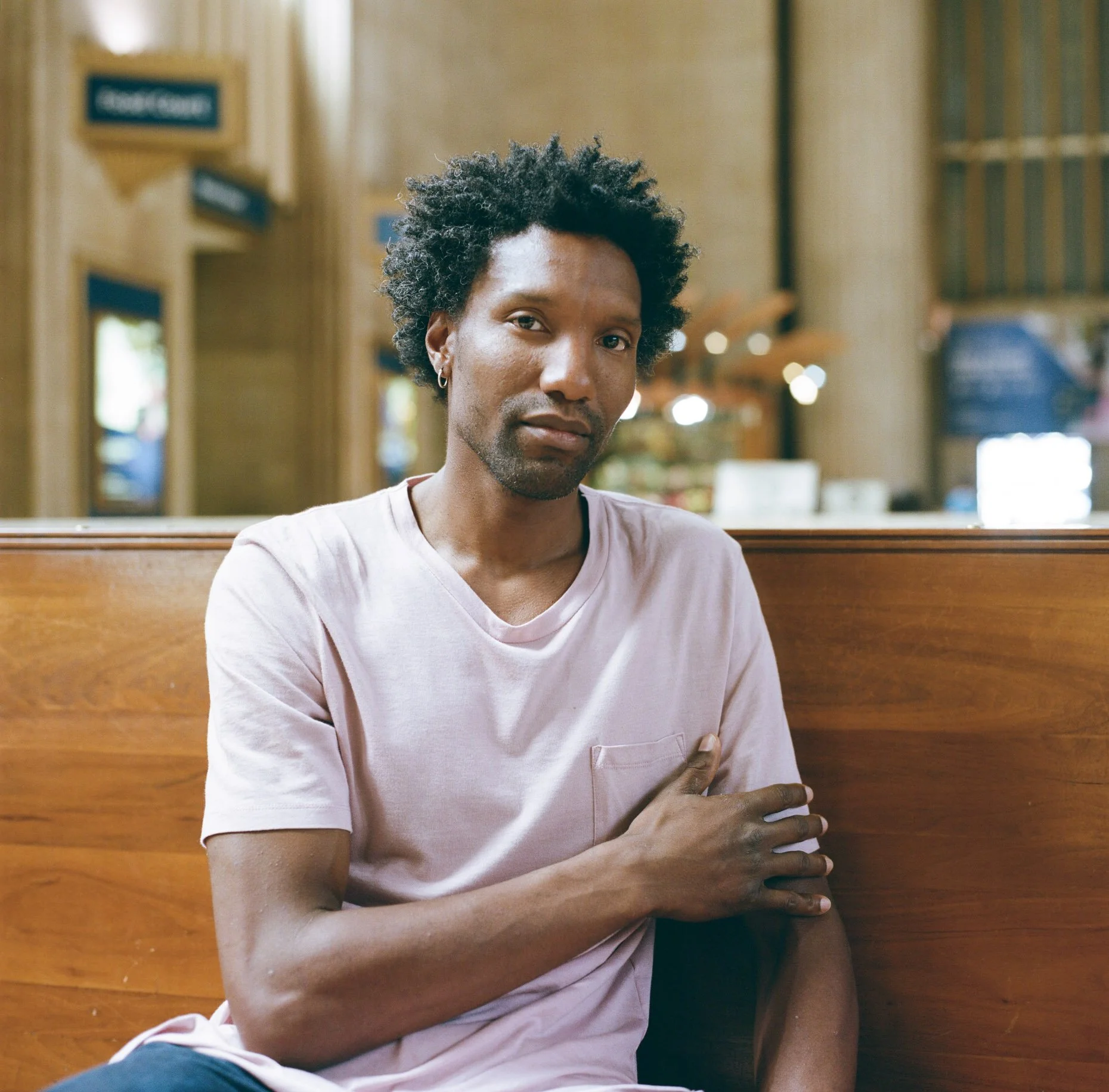 Environmental portrait of a man with natural textured hair sitting in a café interior, warm ambient light and shallow depth of field, photographed in New York City.