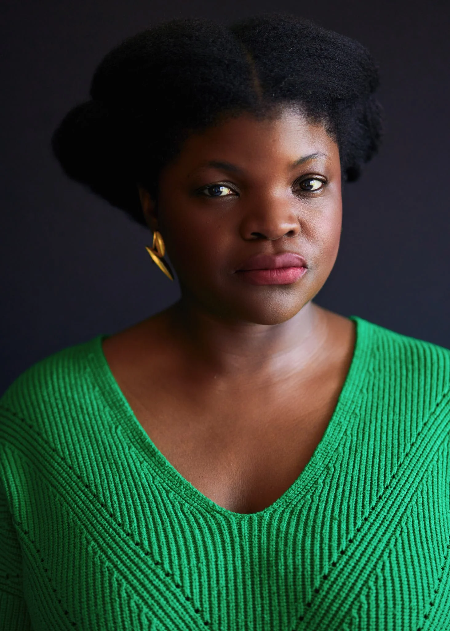 Actor headshot of a woman wearing a green knit top against a dark studio background, direct gaze with soft directional lighting and shallow depth of field, photographed in New York City.
