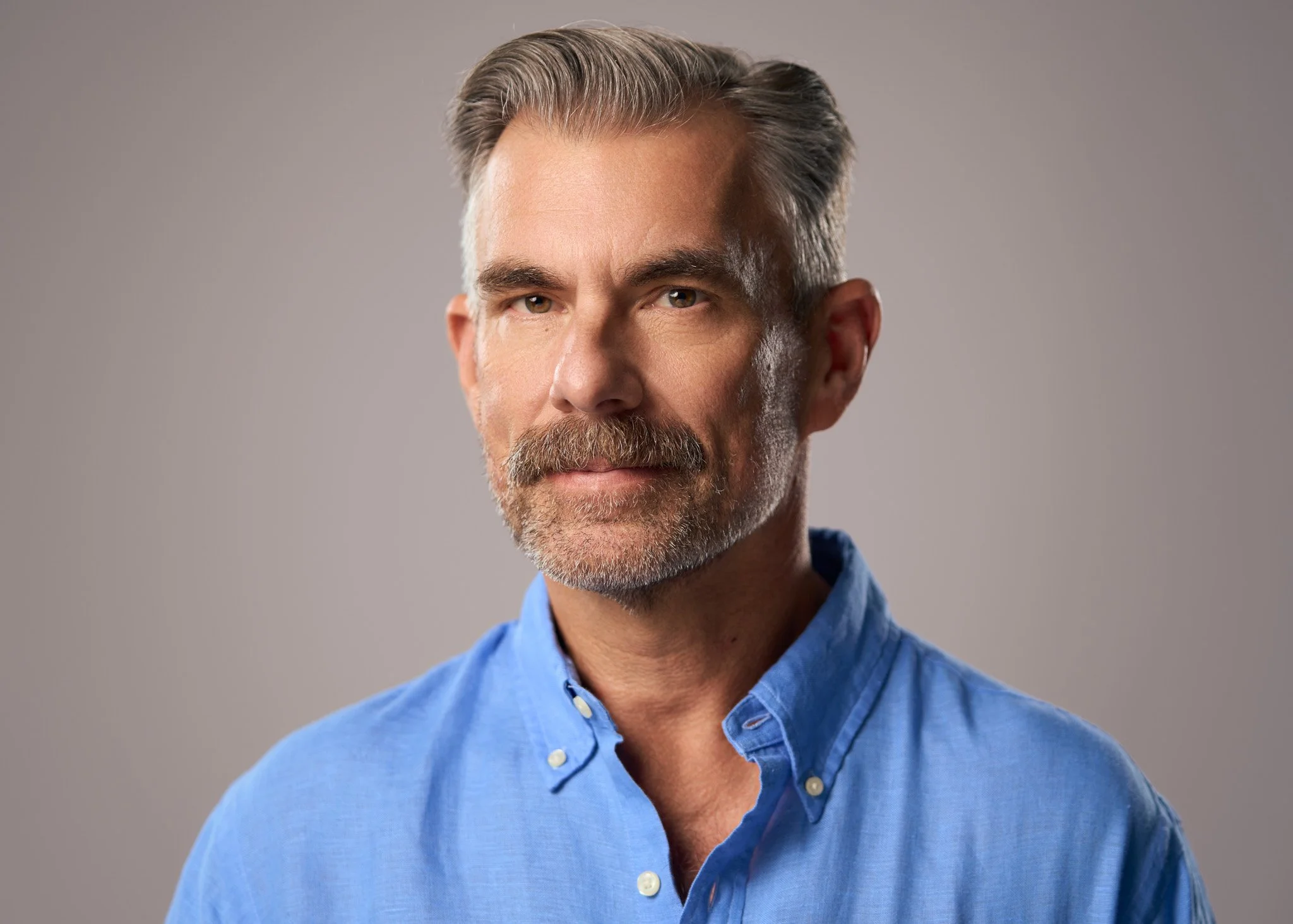 Studio portrait of a middle-aged man with gray hair and a beard photographed in New York City against a soft gray background