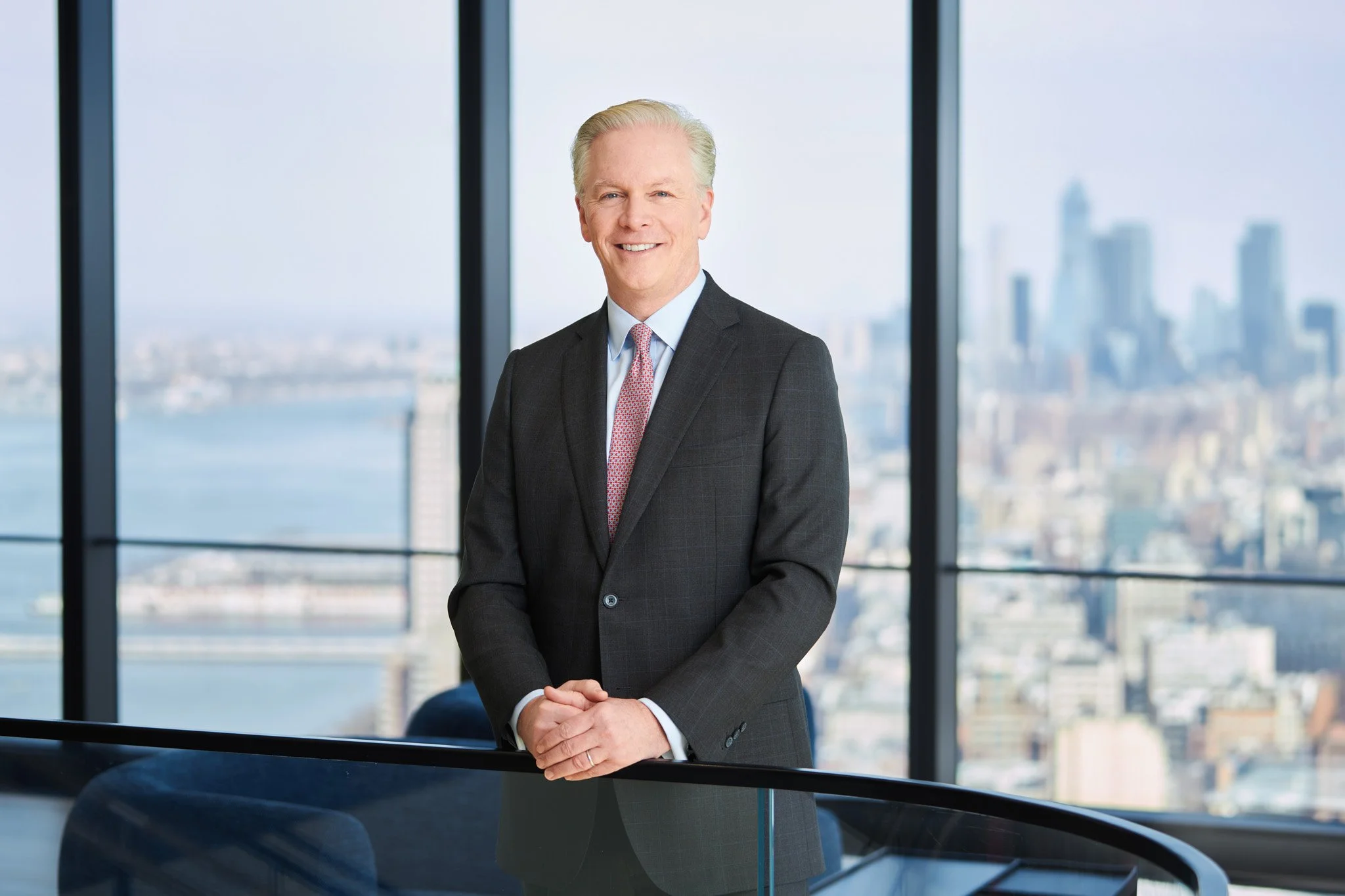 Portrait of a senior partner for a law firm standing by a window with New York City visible in the distance