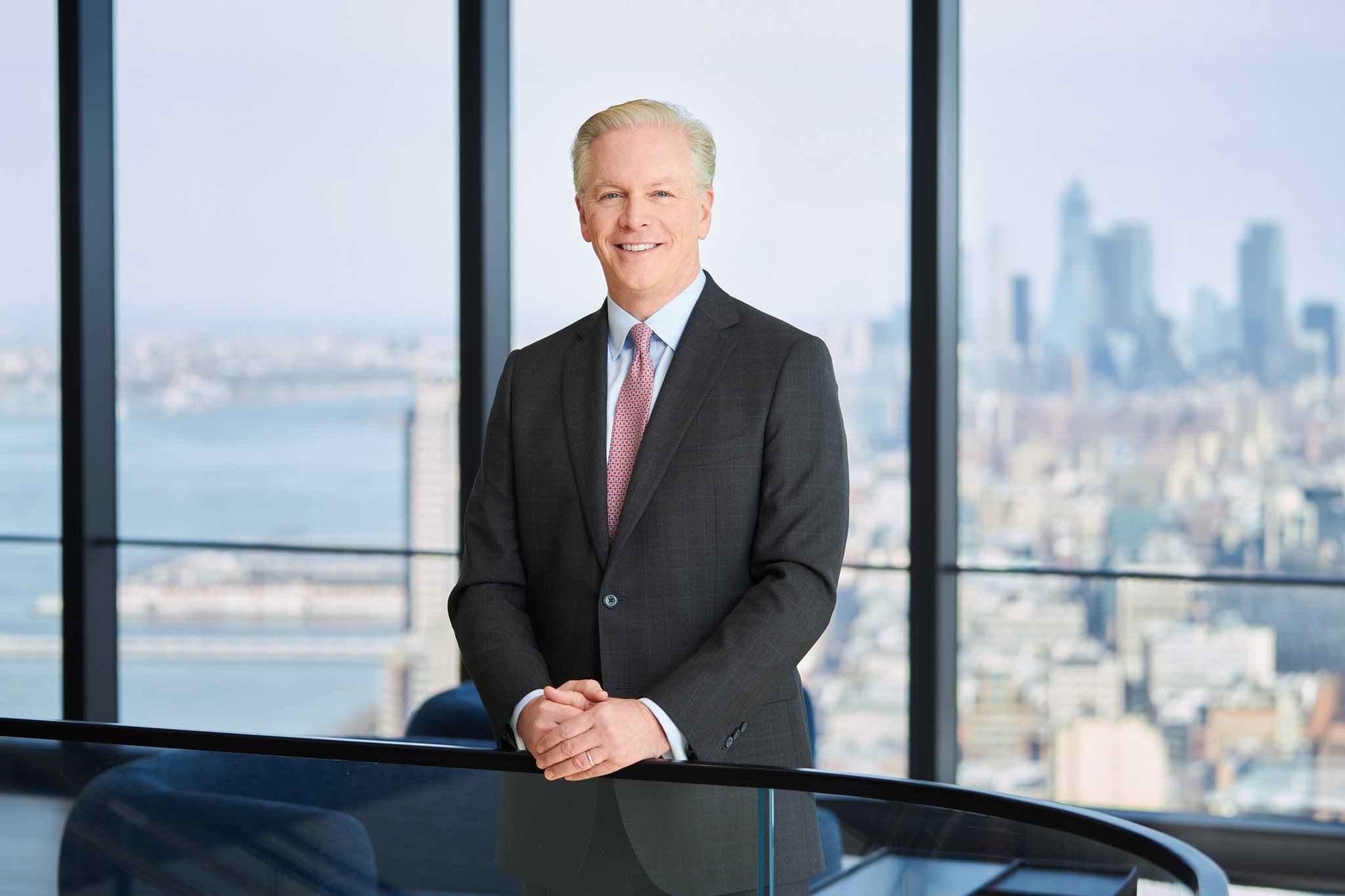 Portrait of a senior partner for a law firm standing by a window with New York City visible in the distance