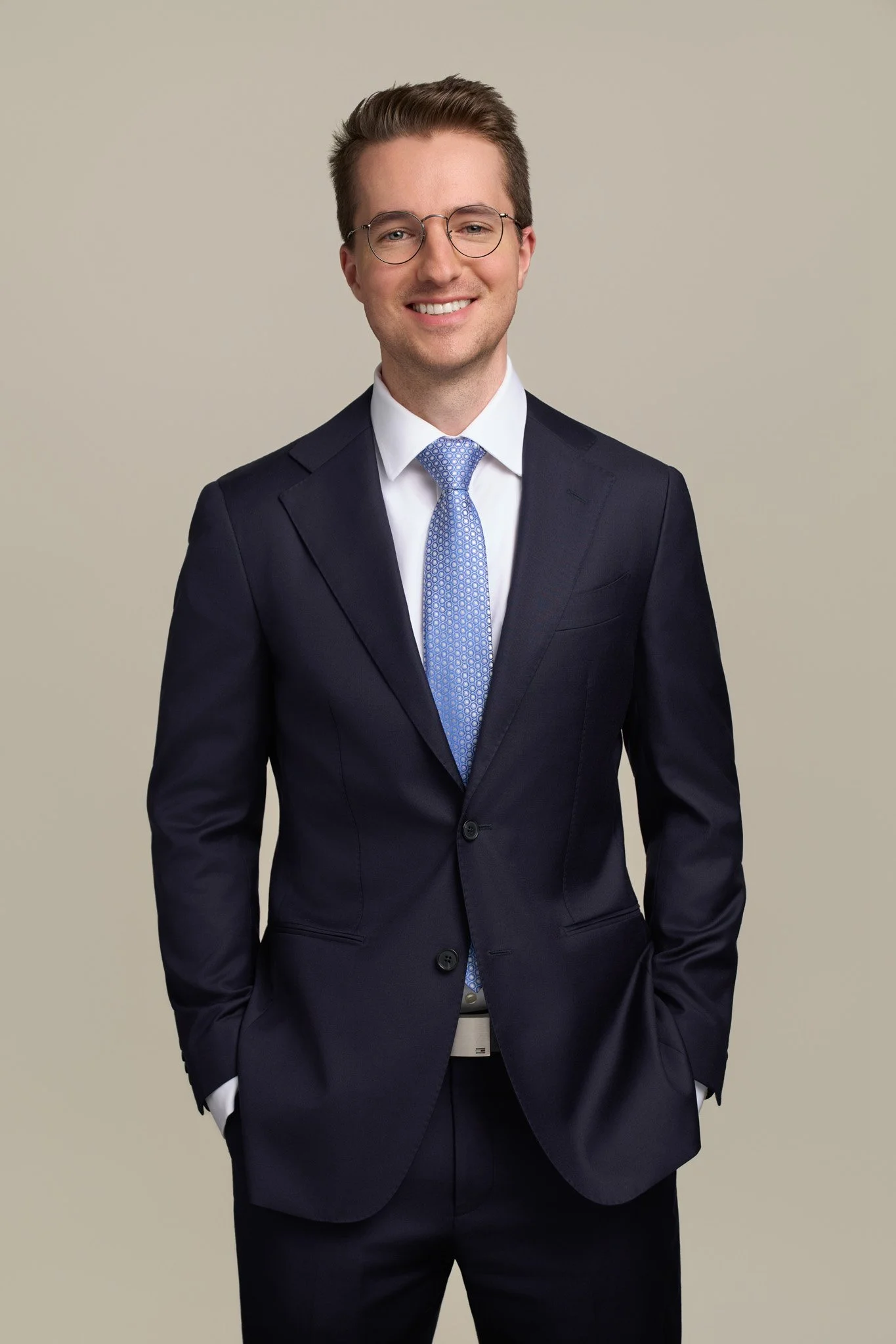 Male professional in a navy suit and light blue tie wearing round glasses, corporate studio headshot photographed in NYC