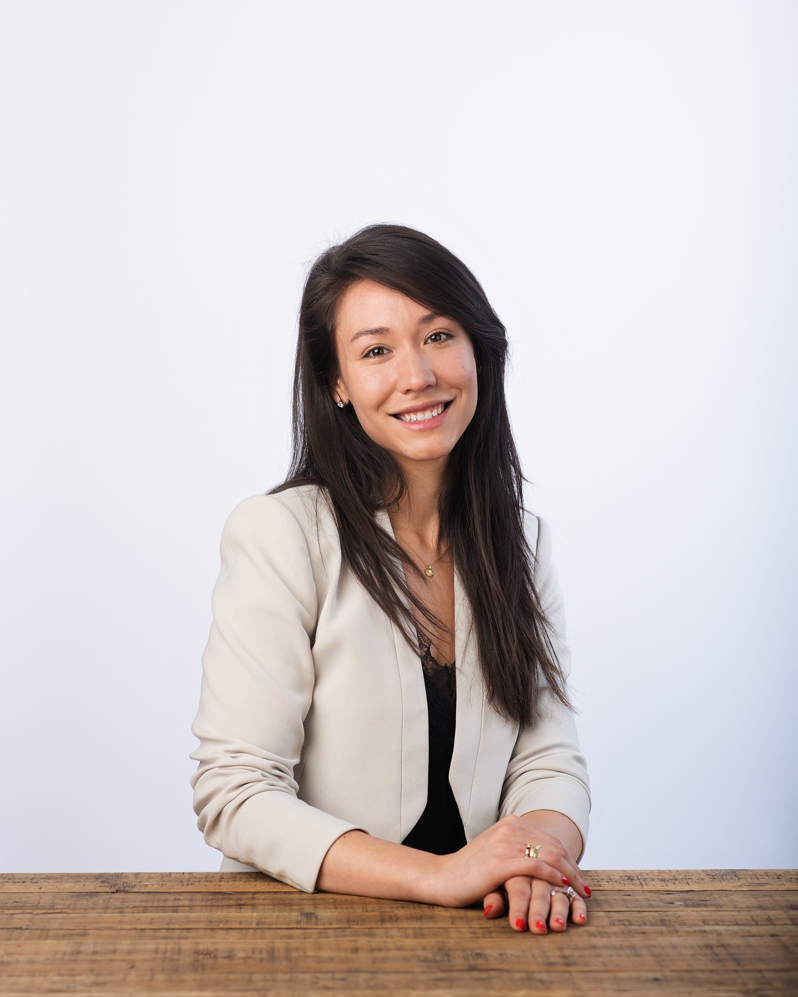 nyc headshots of a woman in a cream blazer seated at a table with soft studio lighting and a relaxed expression