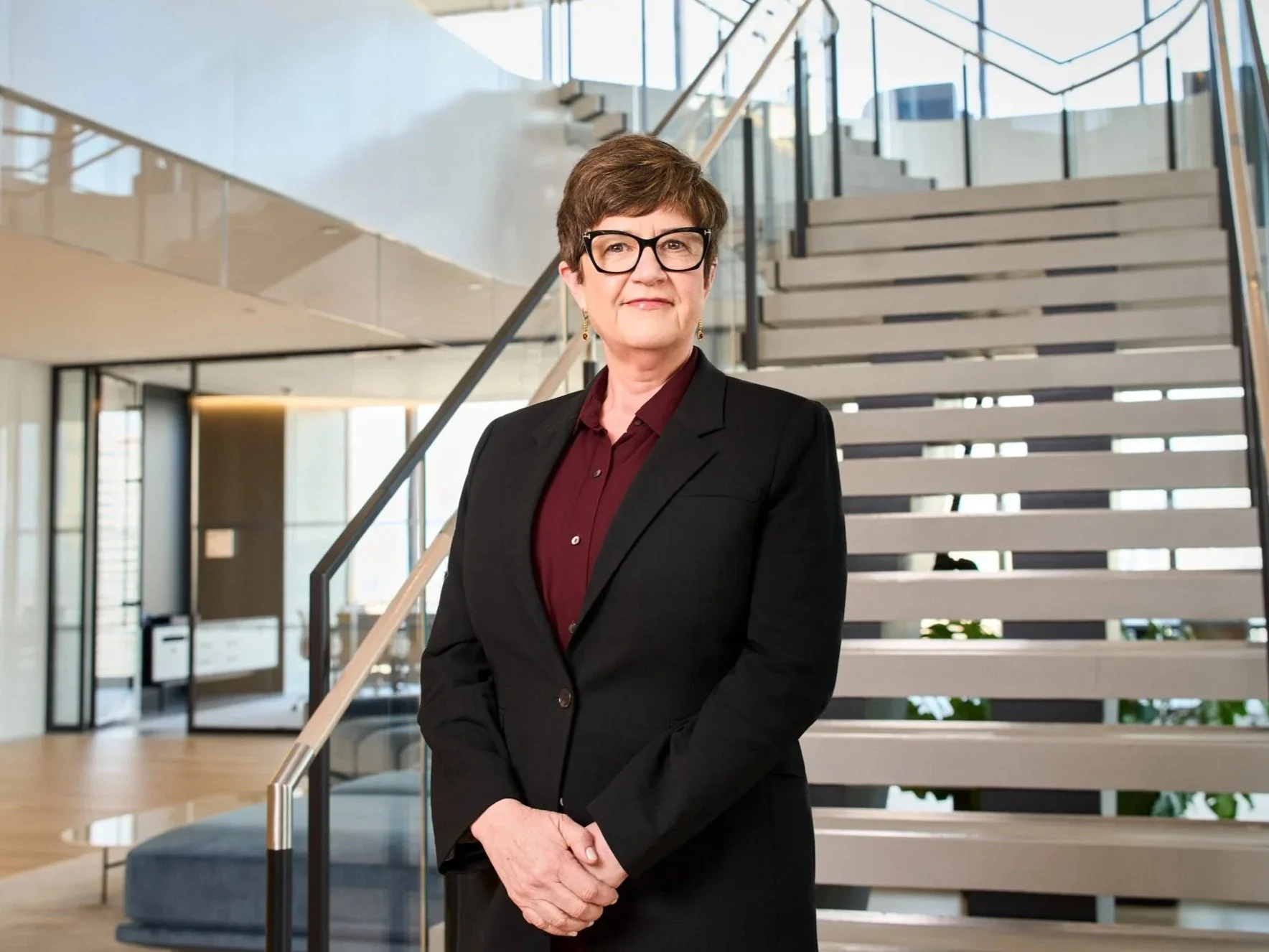 Female executive in black blazer and glasses on a modern office staircase, professional headshot photographed in New York City