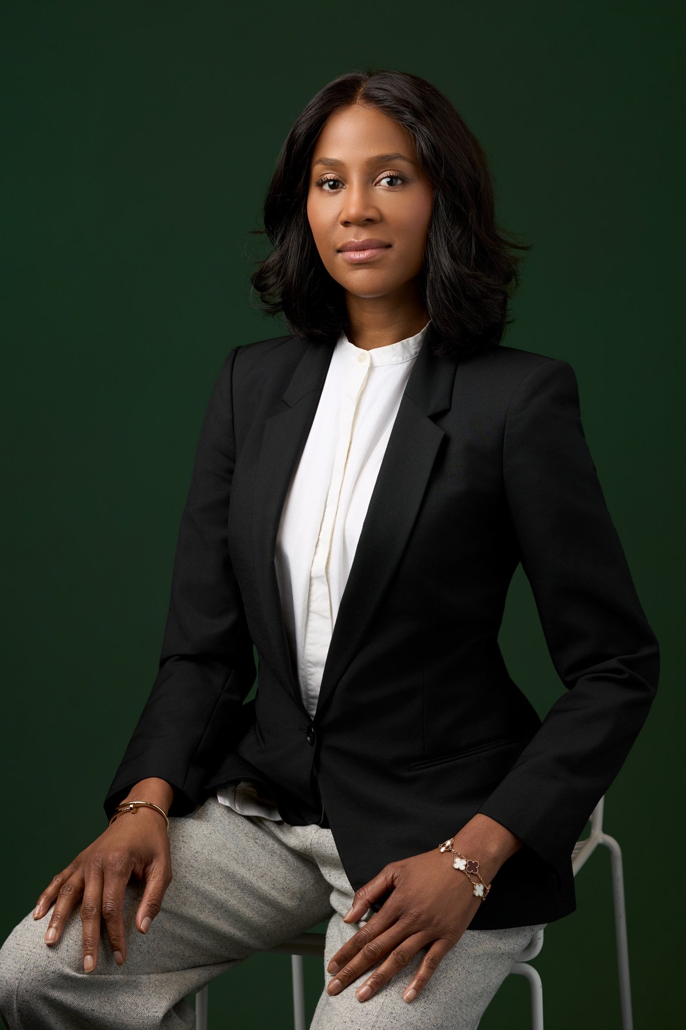 Corporate portrait of a woman photographed in New York City, seated in a clean studio setup against a dark green background. 