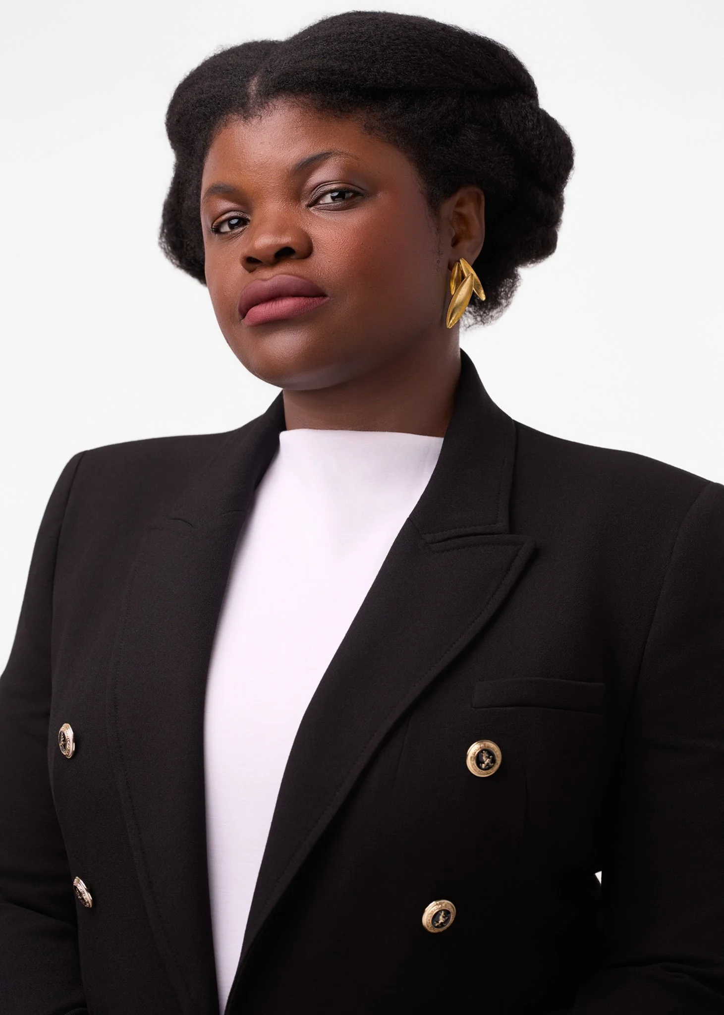 Professional studio headshot of a woman wearing a black blazer and gold earrings against a clean white background, soft even lighting, photographed in New York City.