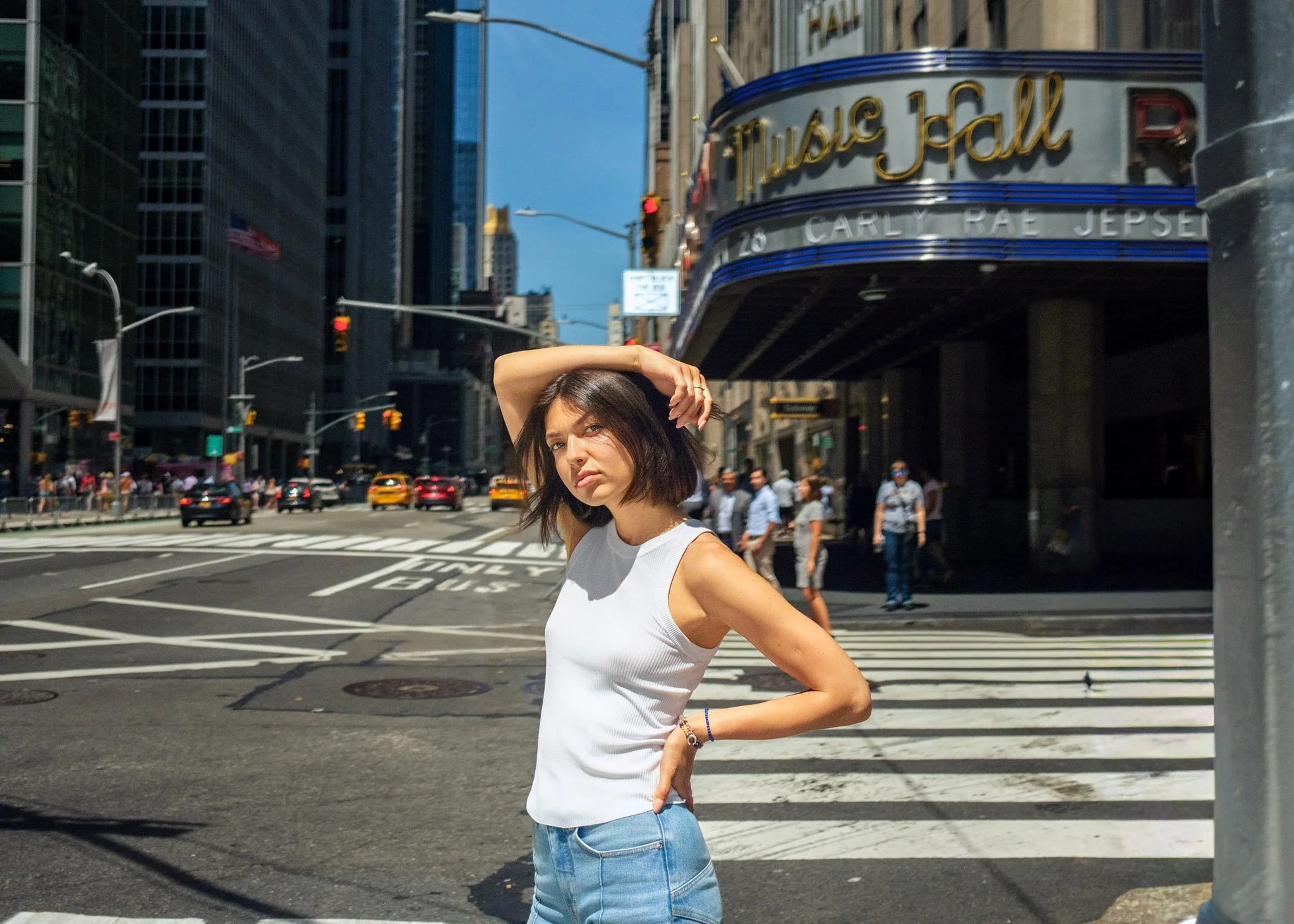 Editorial street portrait of Daria Shevchenko outside Radio City Music Hall in Manhattan, photographed in bright midday NYC light with city traffic and crosswalk in the background.