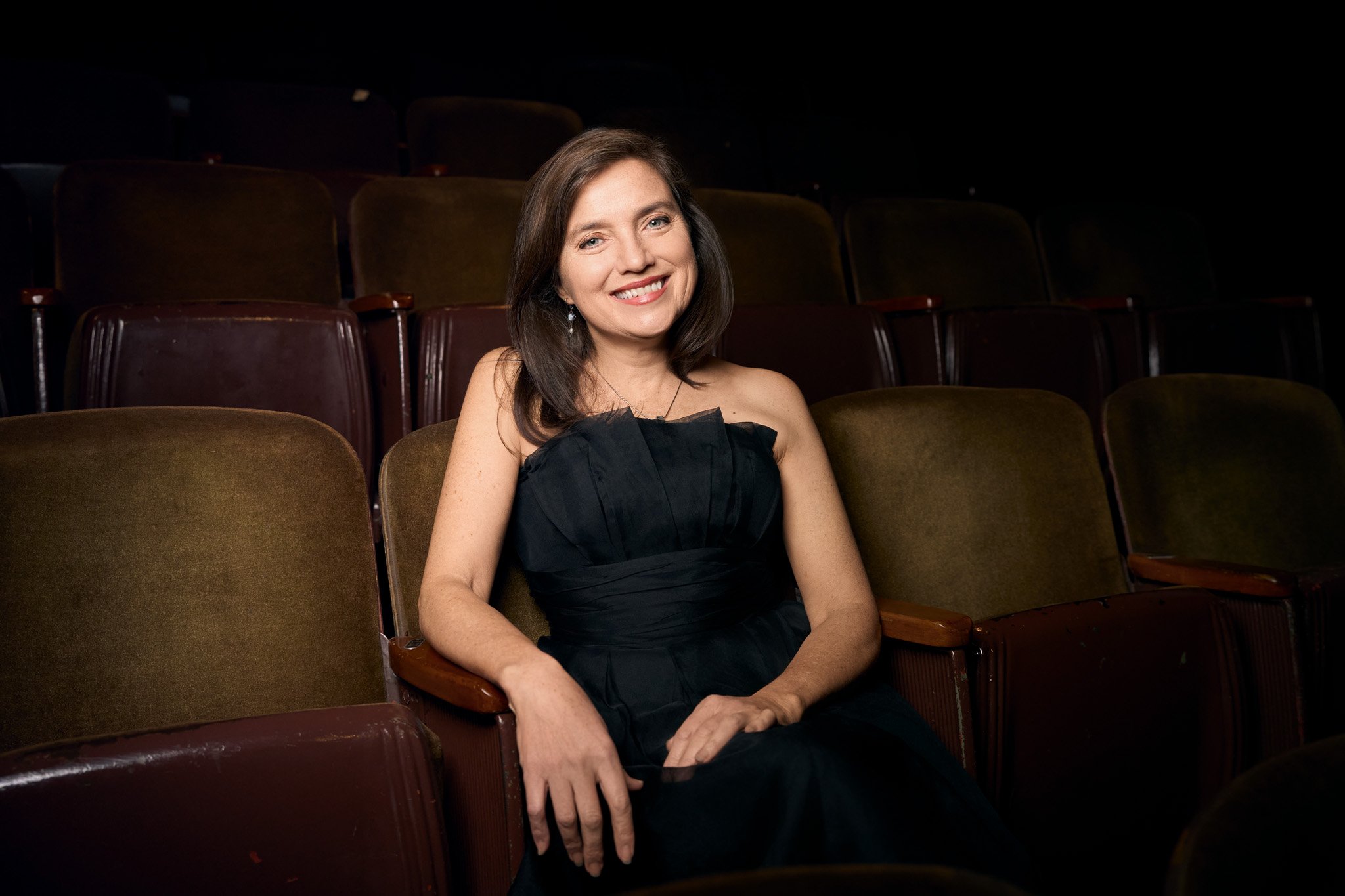 Editorial portrait of a woman seated alone in an empty theater, photographed in New York City with low, dramatic lighting
