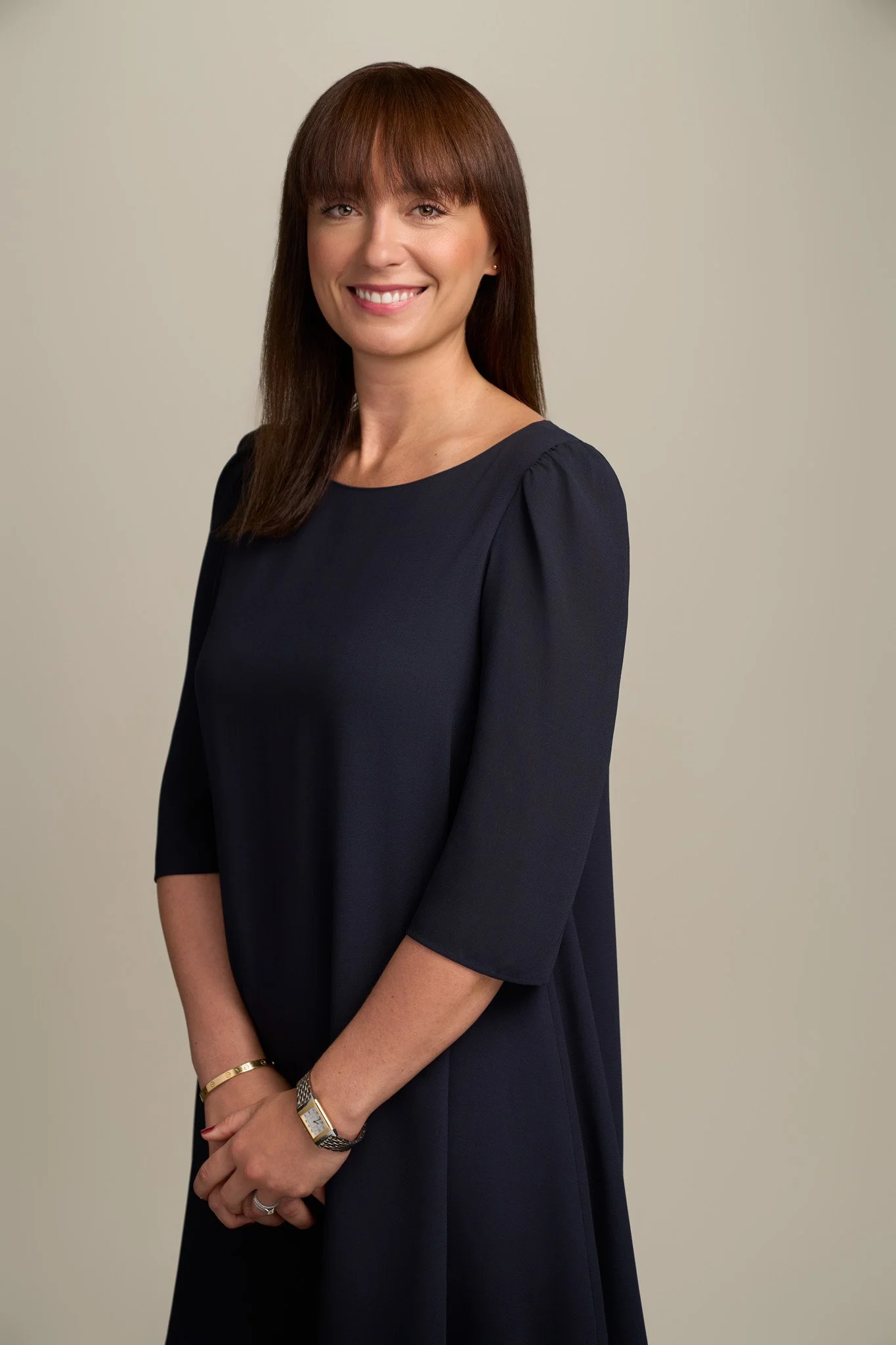 Smiling female executive with brunette hair in a navy dress, studio headshot photographed on neutral backdrop in New York City