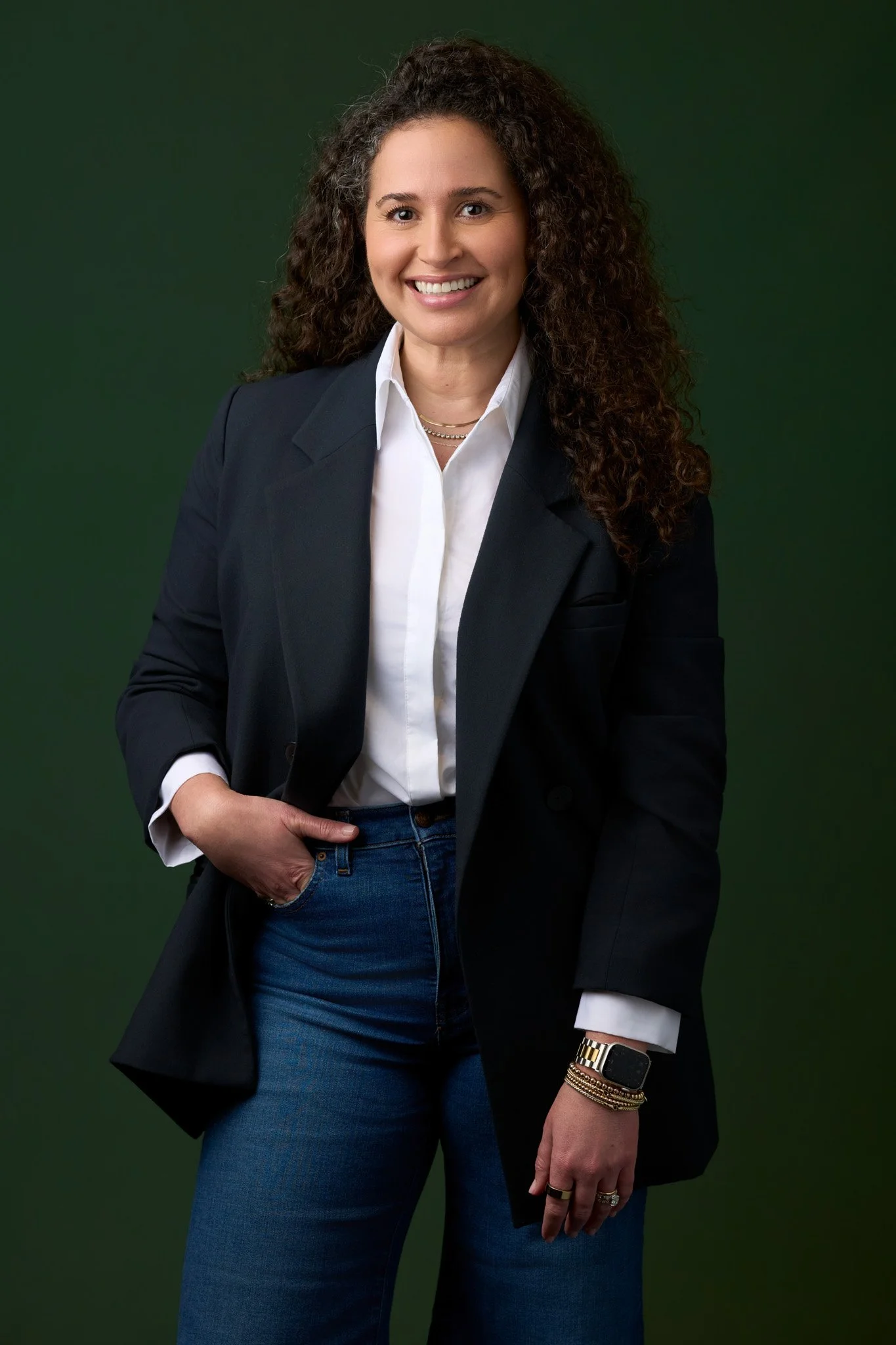 Female executive in a black blazer and white shirt against a deep green studio background, professional headshot photographed in NYC