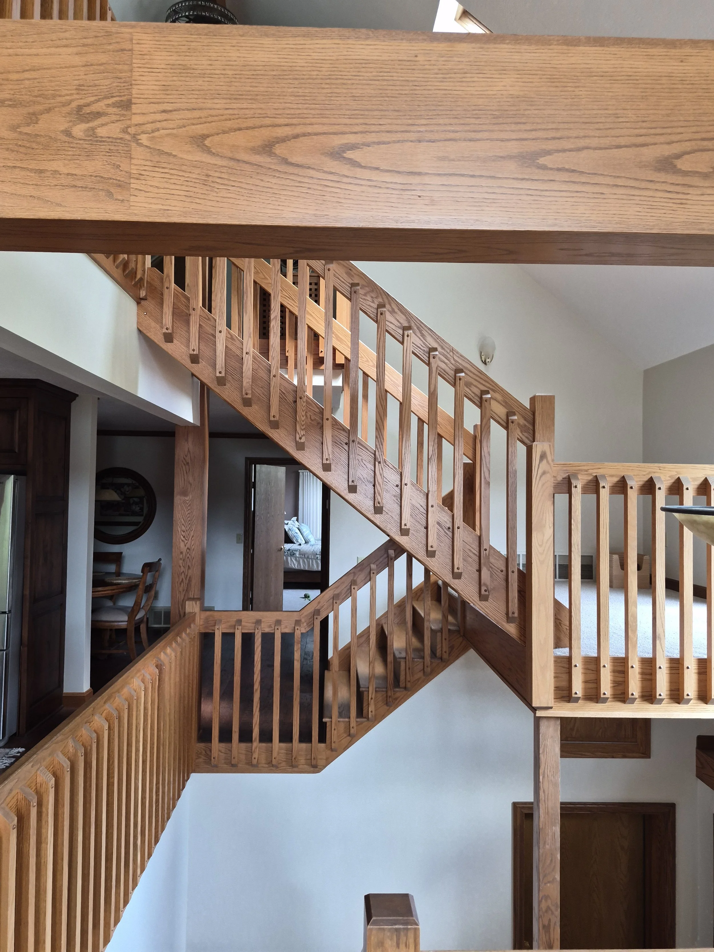 View of a staircase made of wood, with railings and a vertical newel post, inside a house with beige walls.