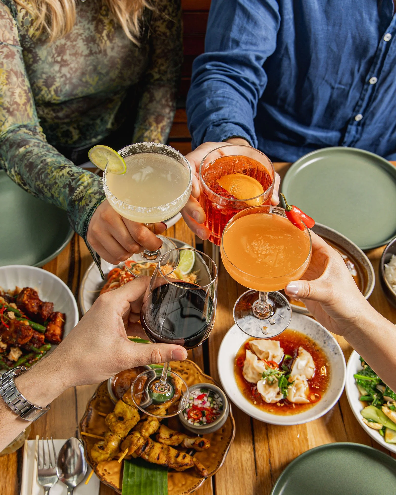 Photo of guests toasting cocktails at Muum Maam over a table of Thai dishes, capturing a vibrant and social dining experience.
