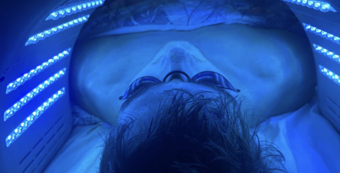 Person wearing protective goggles in a blue-lit tanning bed