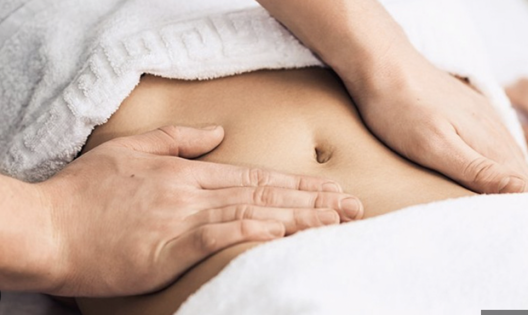 Hands massaging the abdomen with a white towel in the background.