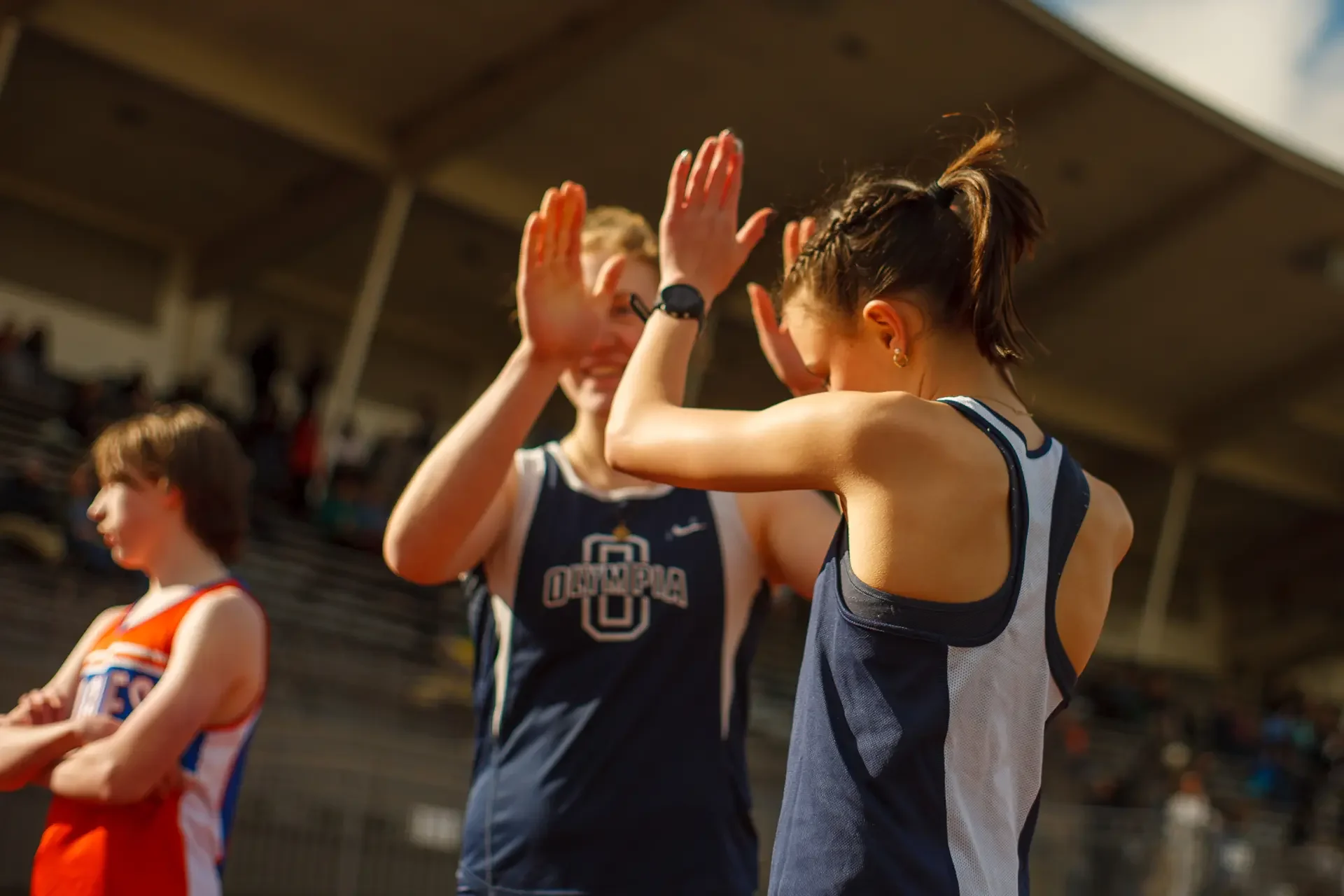 Two high school track athletes in blue and white jerseys exchange a high five on a track at Olympia High School, photographed by Russell Moore.