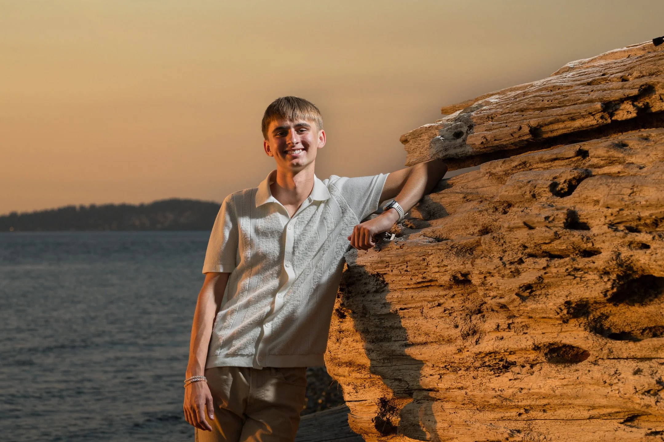 Curtis High School senior Asher Pepin leaning against driftwood at sunset, senior portrait session at Chambers Bay, University Place, Washington