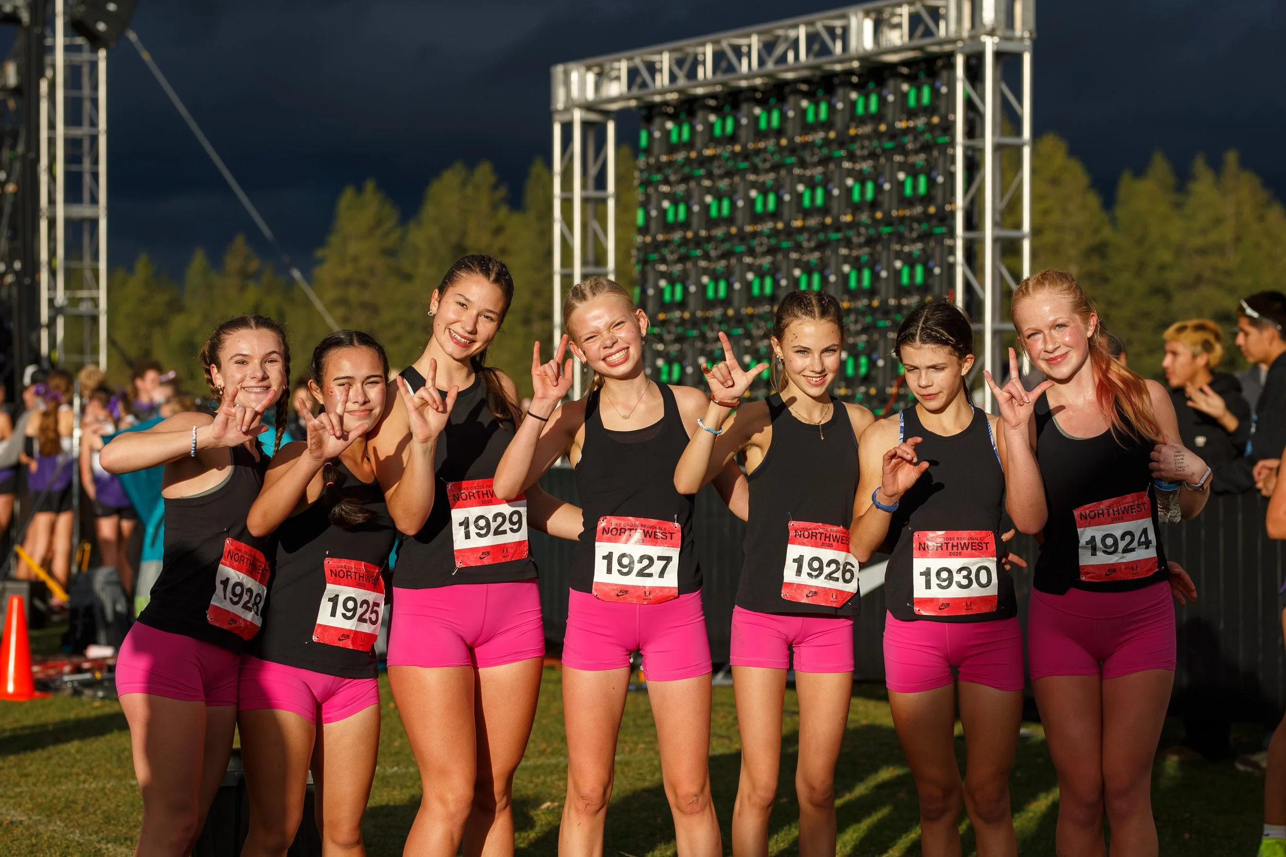 The Olympia High School girls cross country team posing together after finishing their race at 2025 NXR Northwest in Spokane, Washington, wearing black and pink uniforms.