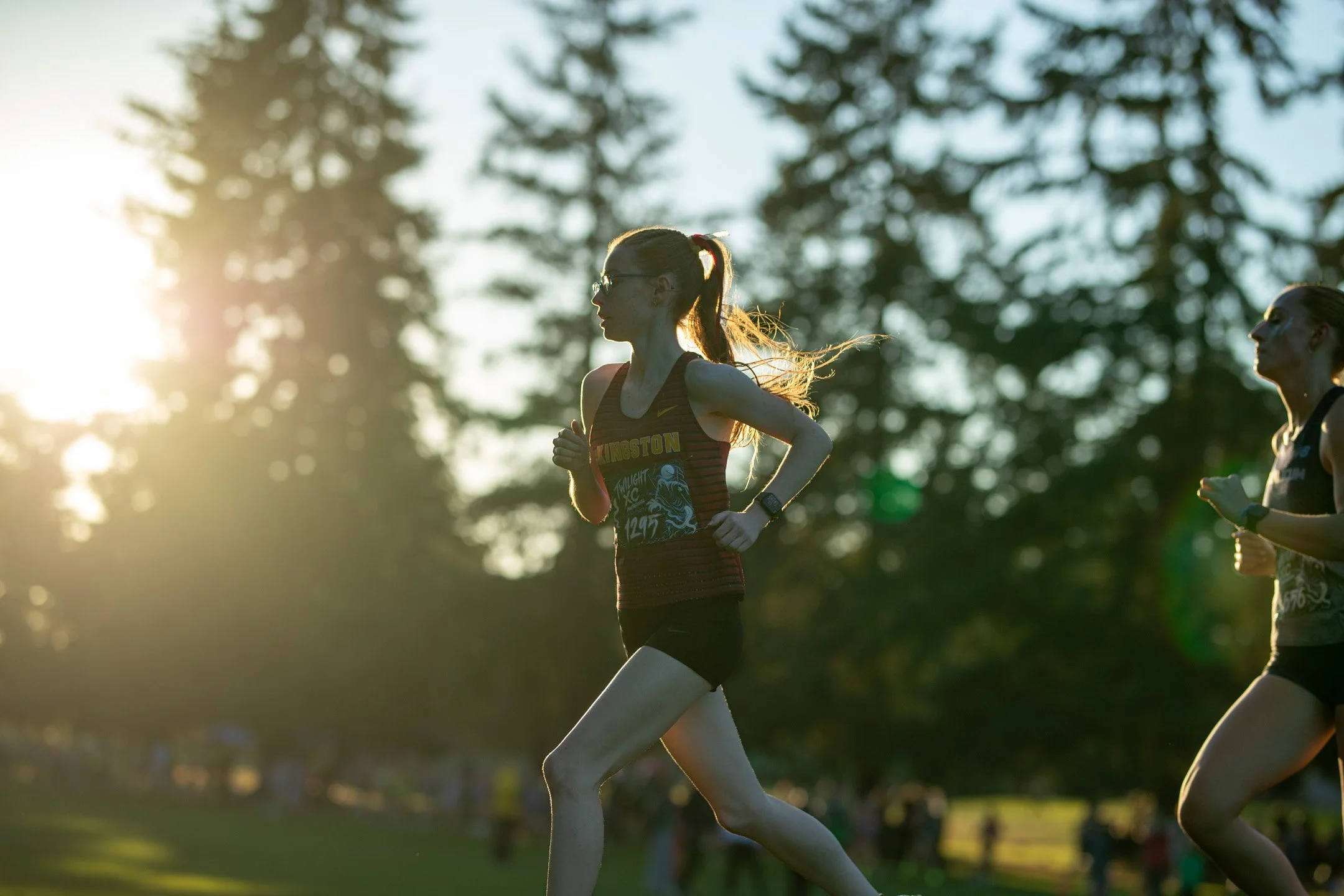 Kingston runner Emma Grice in profile illuminated by a warm golden sunflare while running across the golf course fairway.