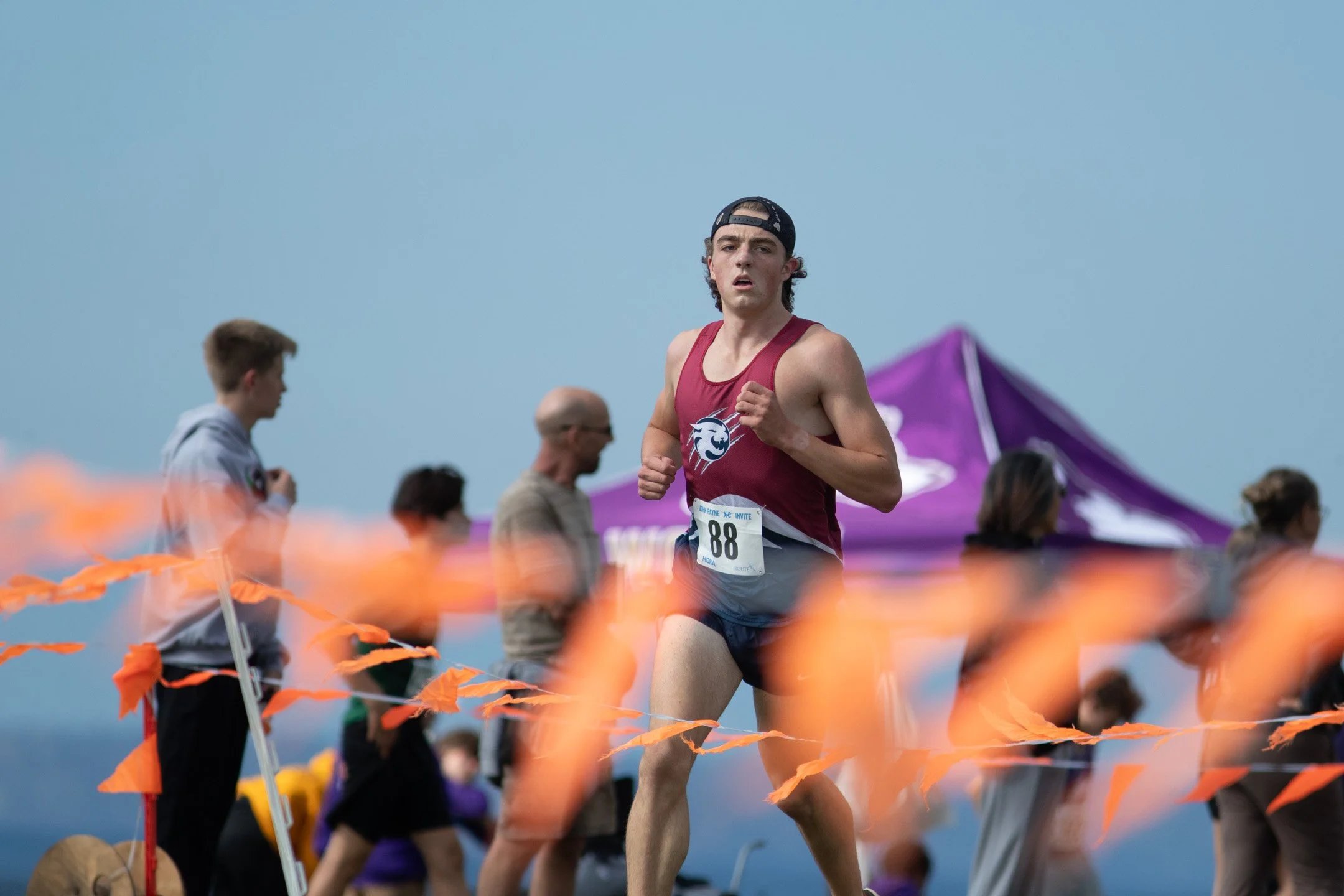 Mt Spokane runner Gatlin Michaelsen in a crimson jersey with bib 88 and a backwards black cap running past orange course pennants.