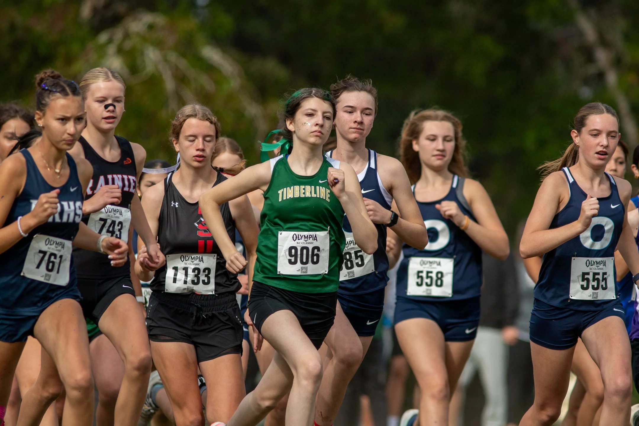 Pack of freshman girls cross country runners sprinting off the start line, one in a green Timberline jersey leading the group.
