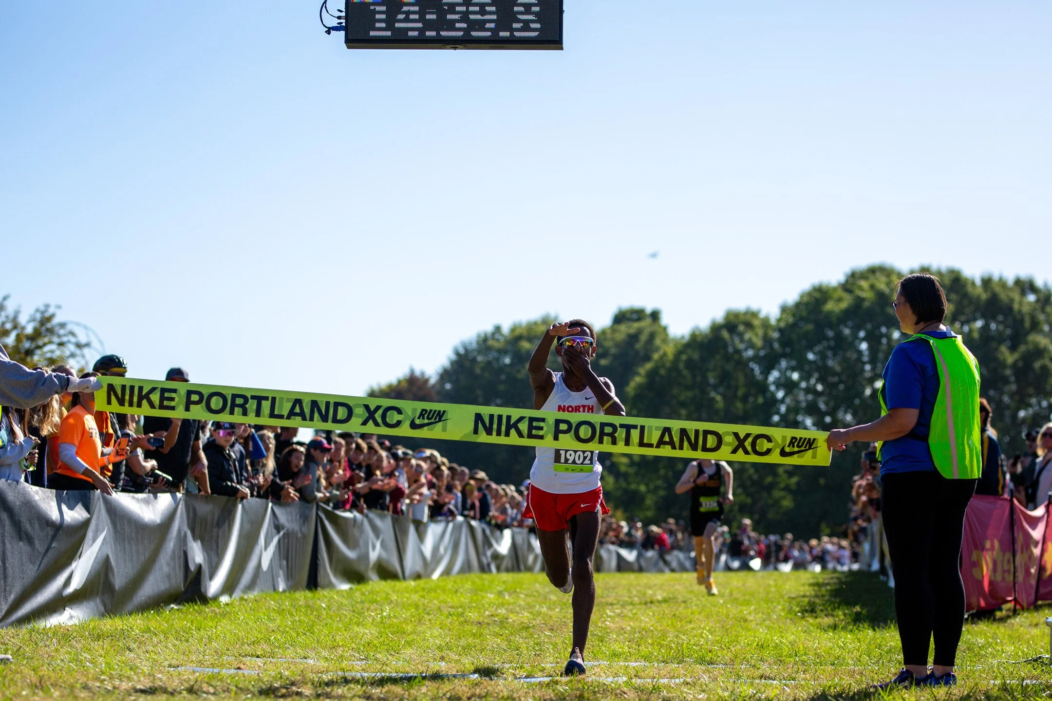 North Eugene's Ashenafi McKinnis, in white, breaks the Nike Portland XC finish tape as spectators line the course.