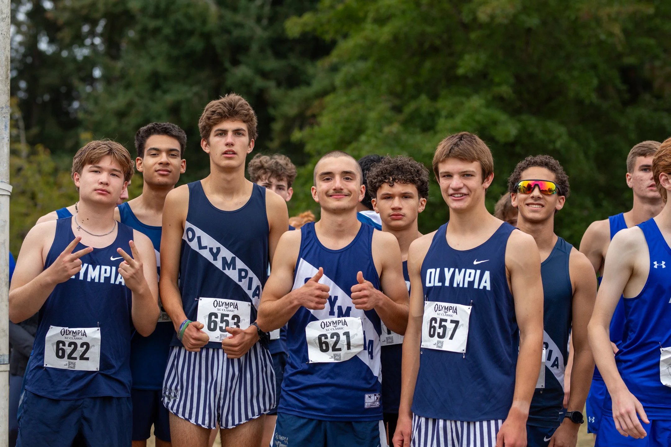 Group of Olympia High School senior boys cross country runners in navy jerseys posing together at the start line before a race.