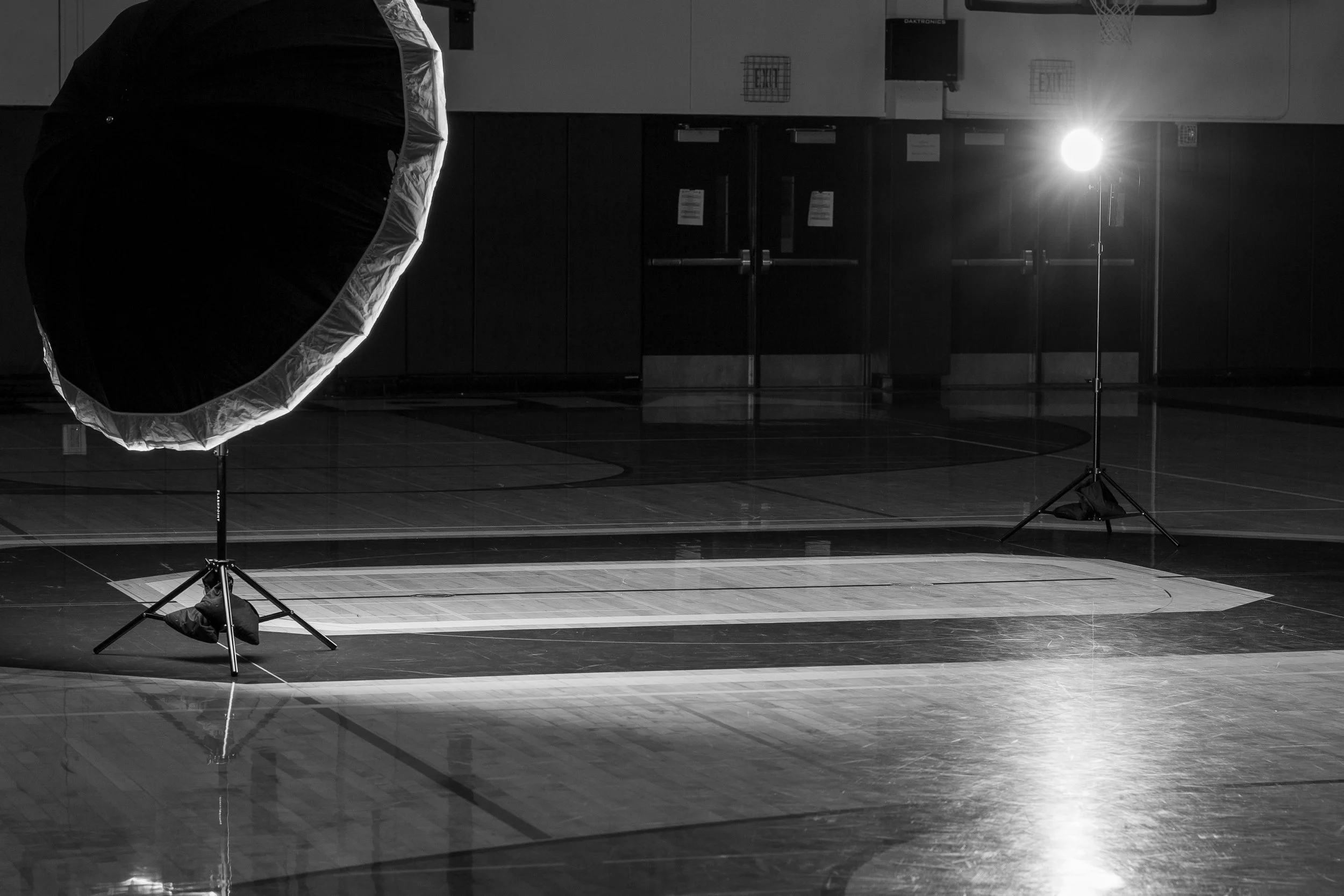 Black and white behind-the-scenes photo of a professional sports photography lighting setup on a dark basketball court in Olympia, Washington.