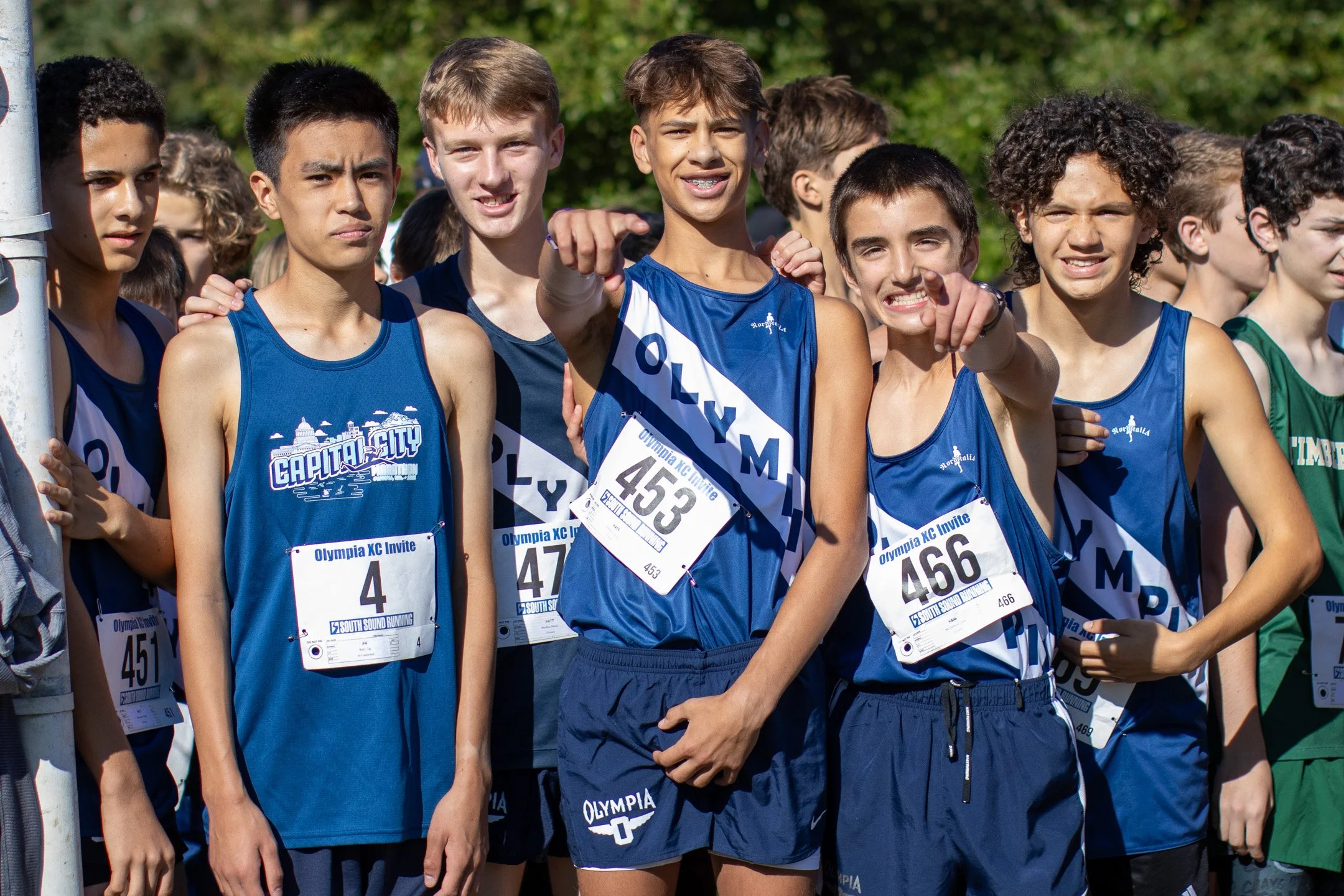 Group of freshman Olympia High School cross country runners in navy jerseys posing together at a race start line, bibs 4, 451, 453, 466 visible.